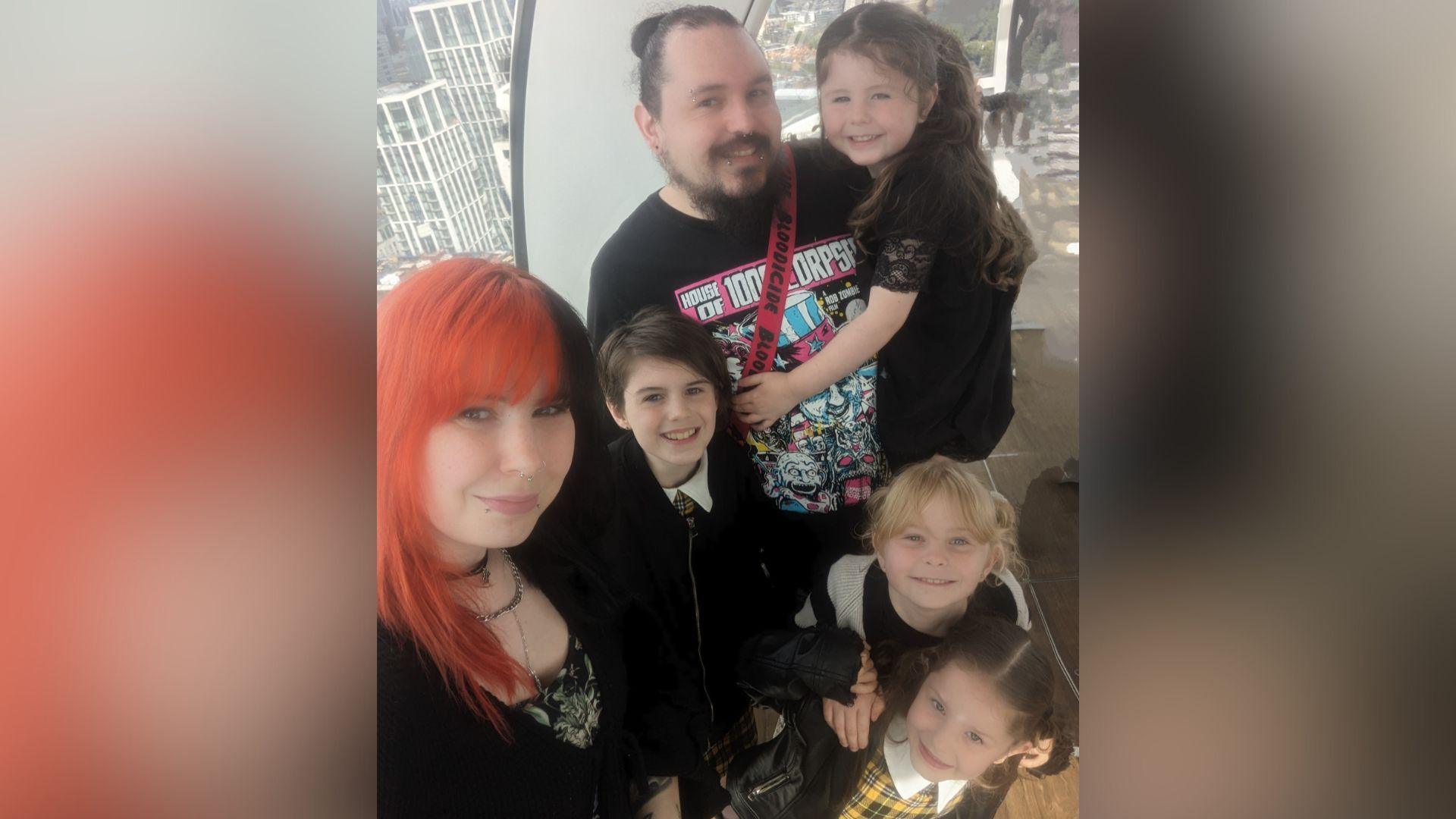 A selfie of Rowan Perry-Lee, who has red and black hair, with her husband and four little girls