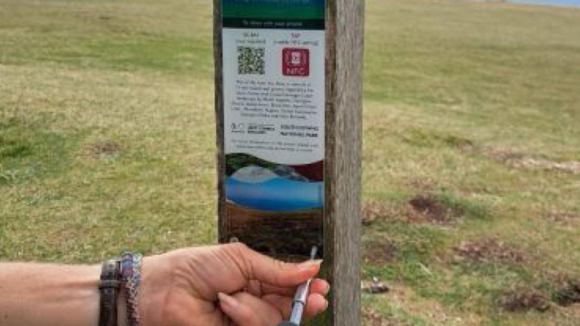 Two hands screwing a blue plaque back onto a wooden pillar with a green field behind it