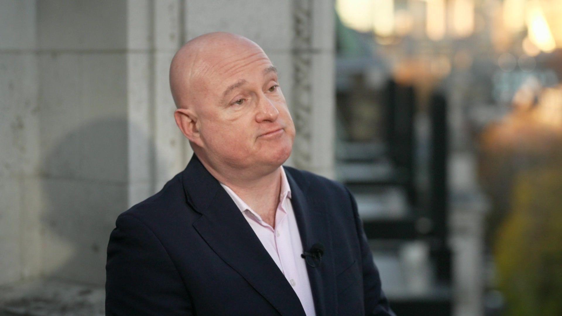 Jack Gilbert wears a suit and shirt as he speaks to the camera outside a building