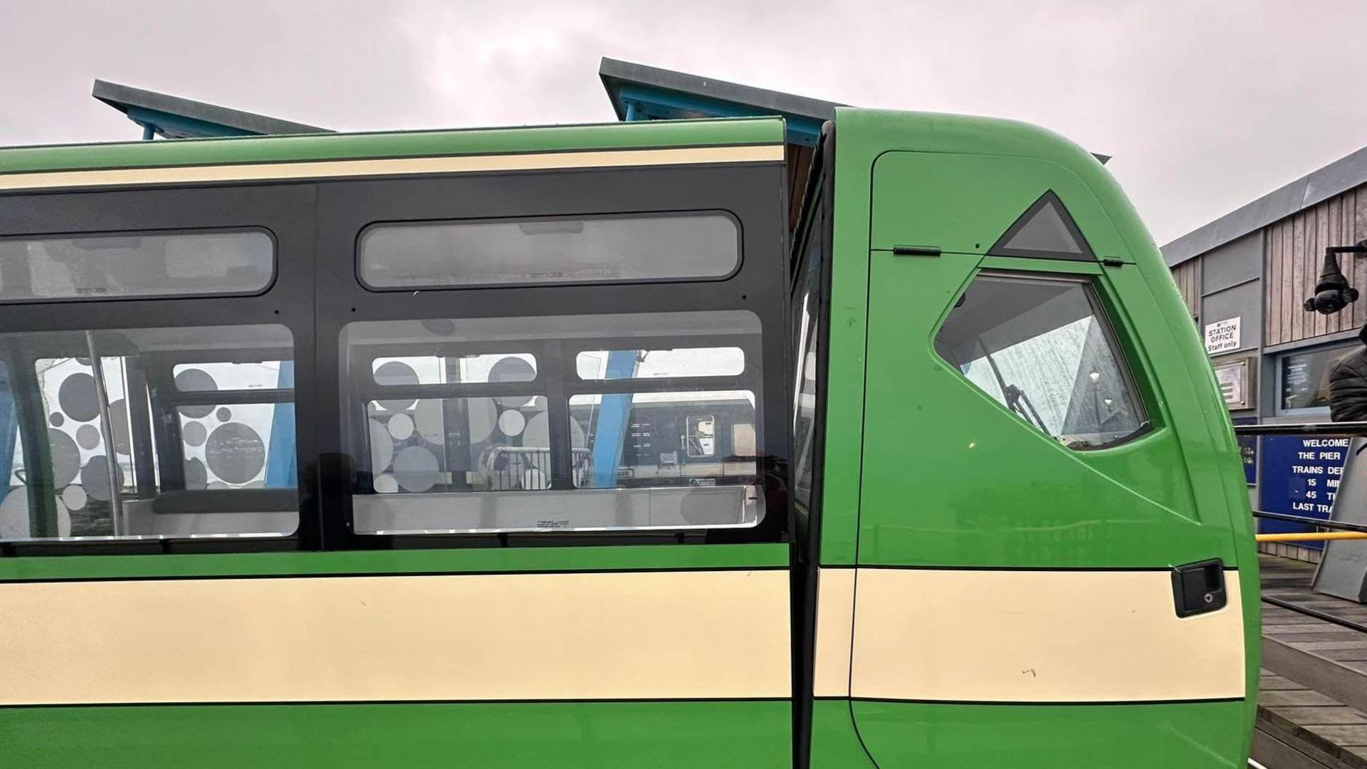 A green train on the pier with a yellow strip running along its side horizontally 