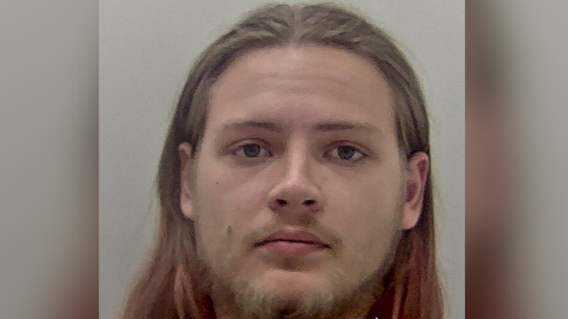 A man with long hair and a beard. His portrait is taken in a police mug shot. 