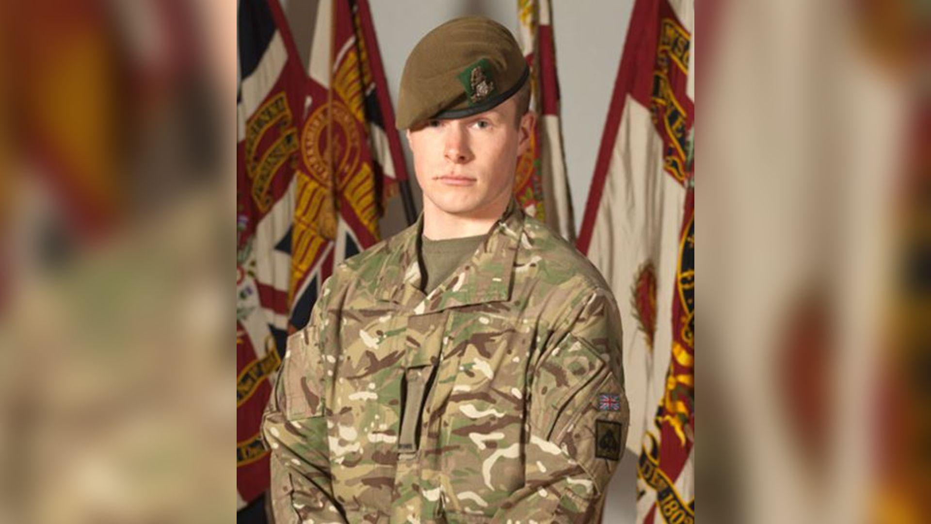 Pte Stone, pictured wearing camouflage military fatigues and green beret of The Yorkshire Regiment. The soldier is stern-faced and has the regimental flag behind him.