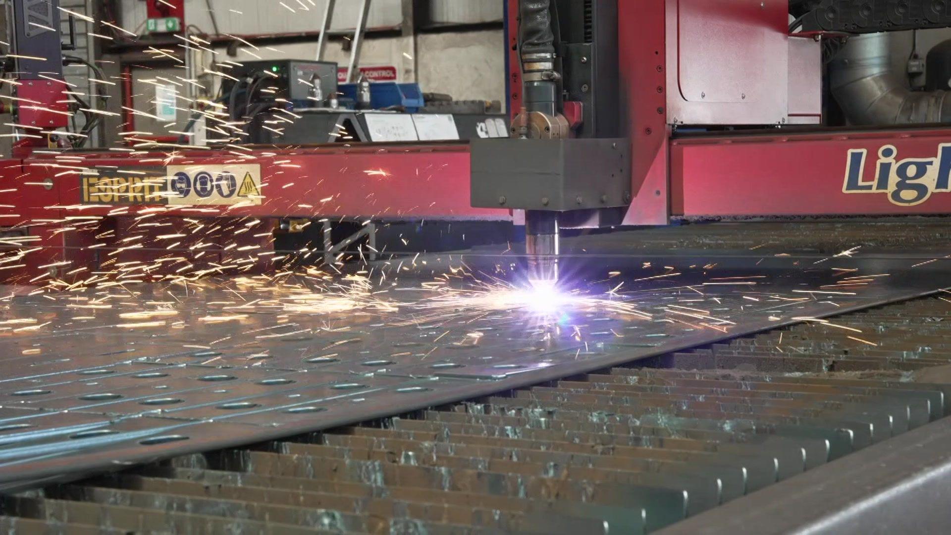 A plasma cutting machine cuts out metal shapes in a factory. Sparks fly 
