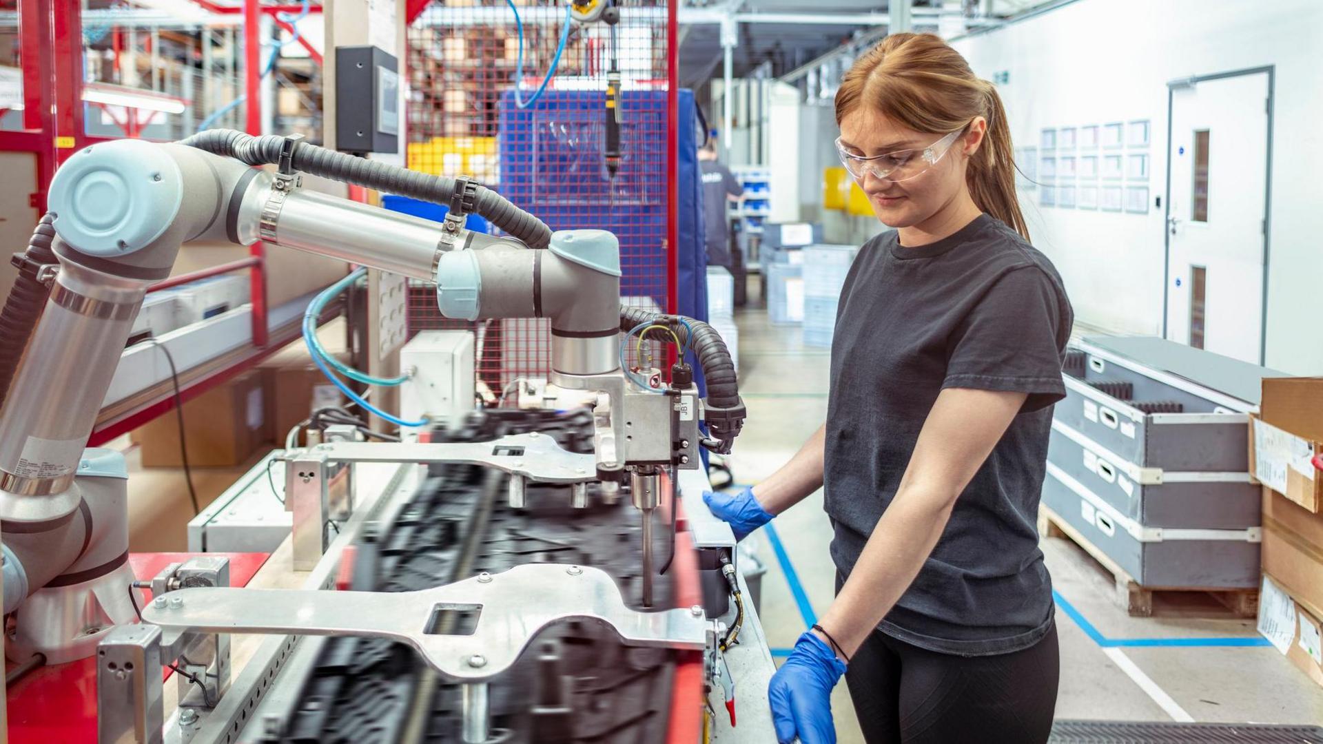 Woman wearing rubber gloves and goggles looking down at manufacturing equipment