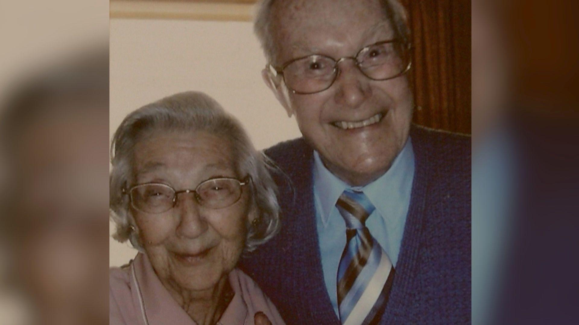 Head and shoulders portraint photo of Gladys and Ron, both smiling to the camera. Gladys has bobbed grey straight hair and Ron has short cropped grey hair. Both are wearing metal rimmed glasses.