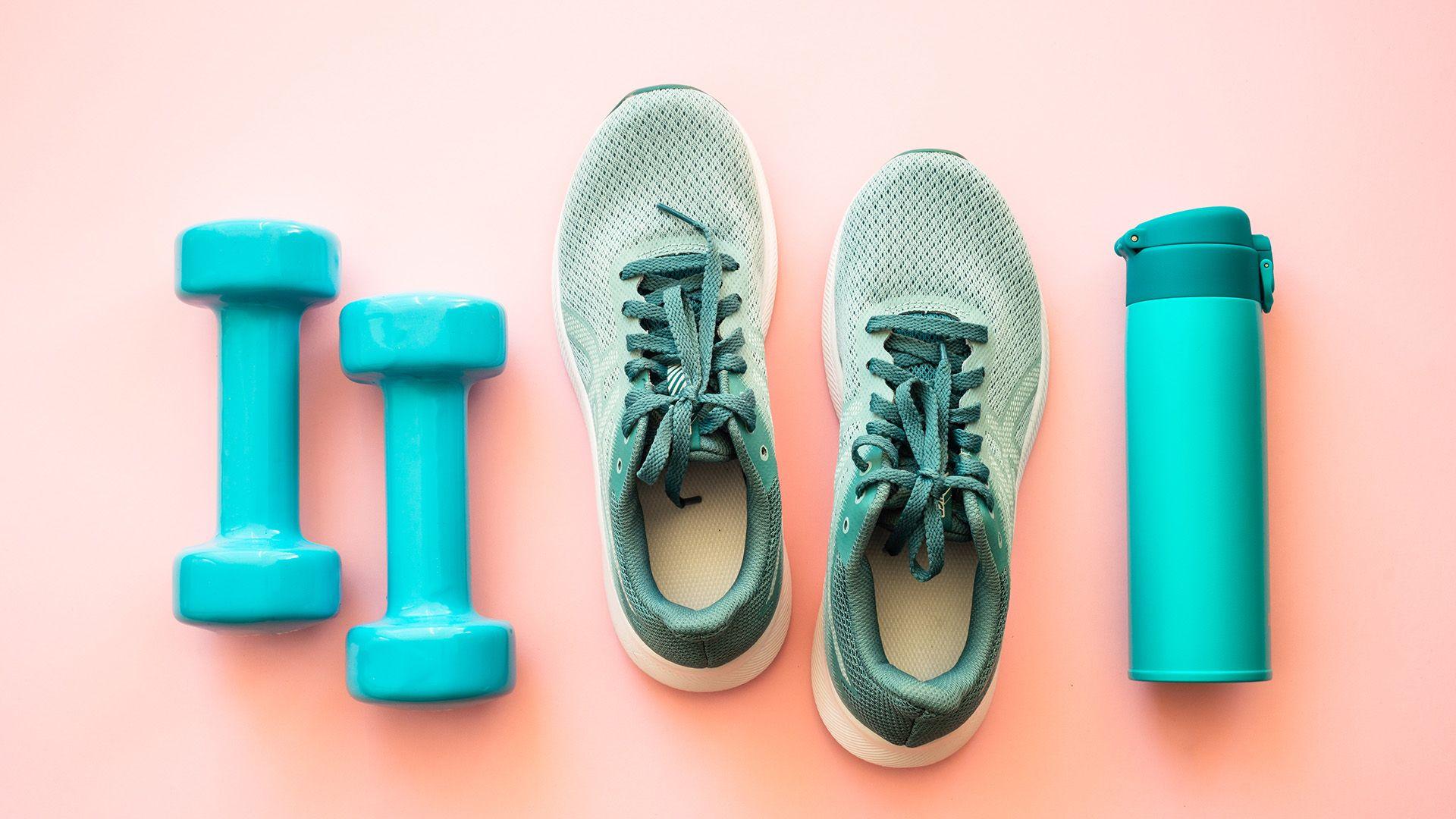 Green trainers, dumbbells and water bottle on a pink background