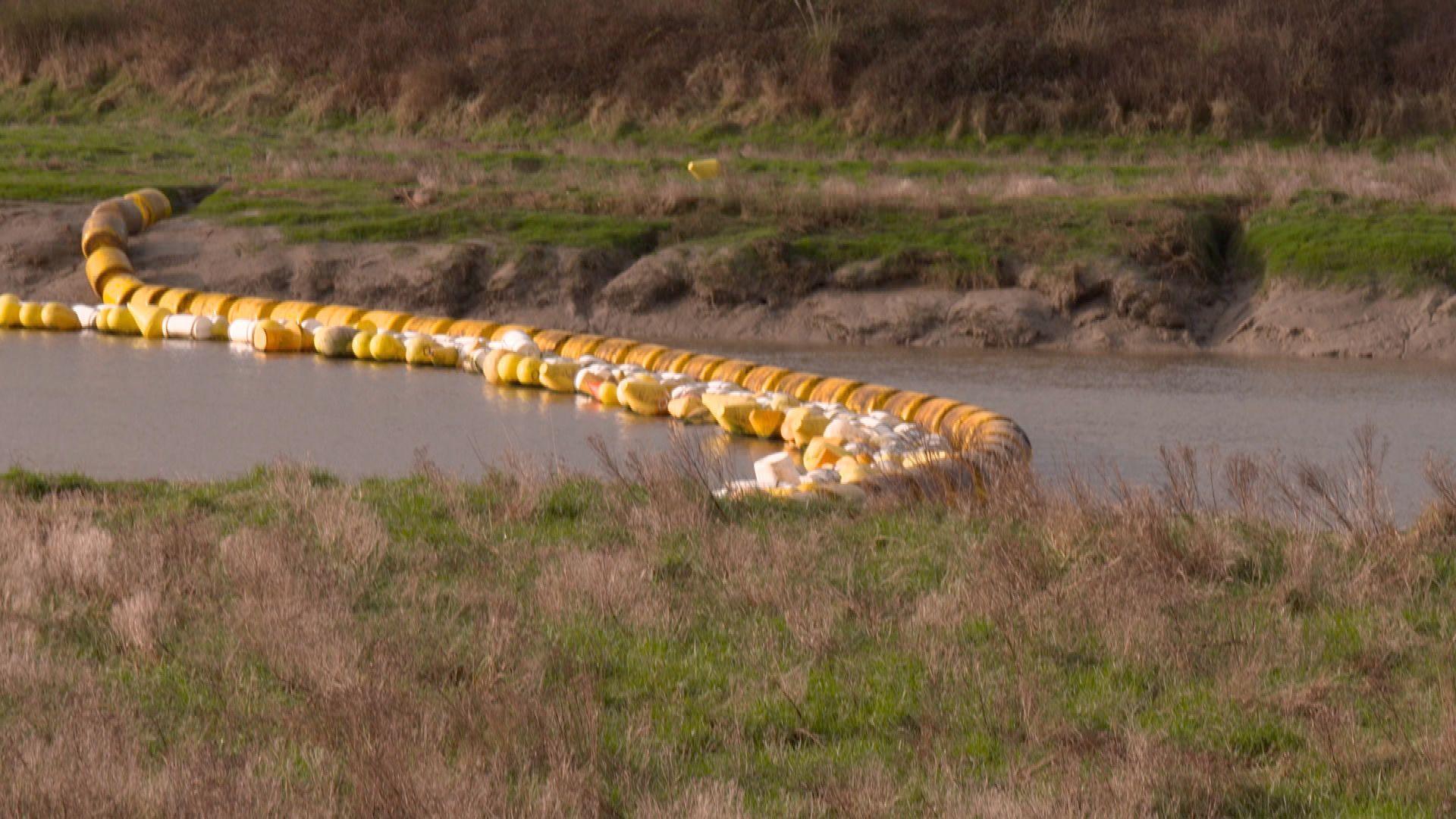 A river blocked with a buoy-like barrier fence that prevents dinghies reaching the sea near Le Touquet 