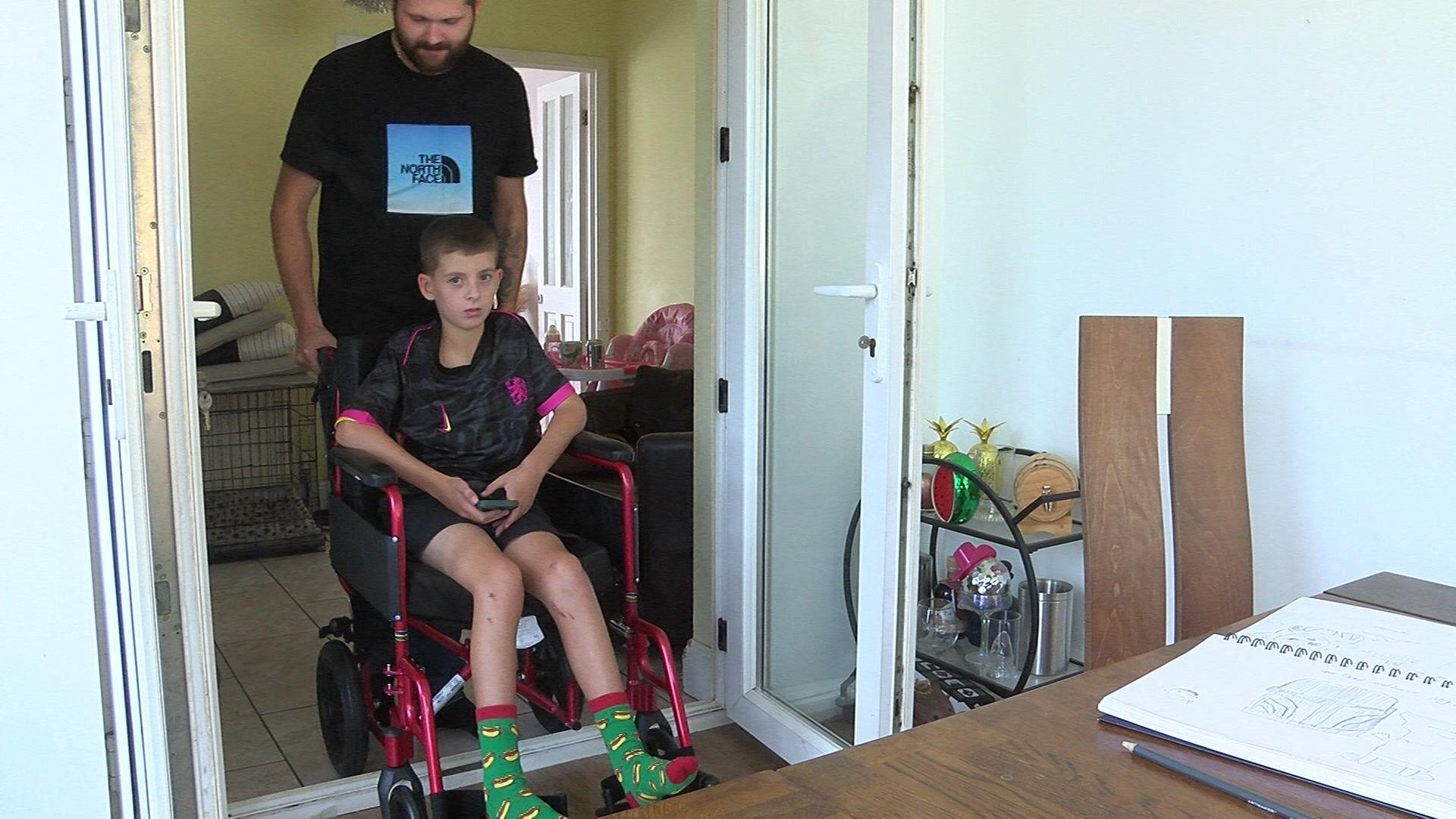 Bradley being pushed in a wheelchair through an open door towards a table