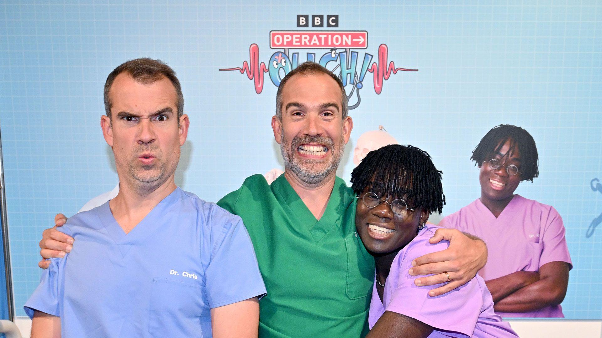 Three doctors smile in different colour medical scrubs.