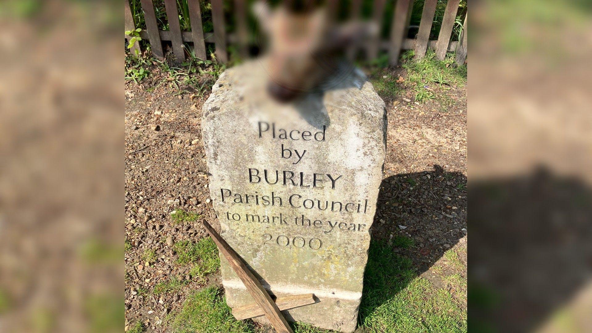 A blurred out deer's head on the memorial stone with an upside down wooden cross at its foot