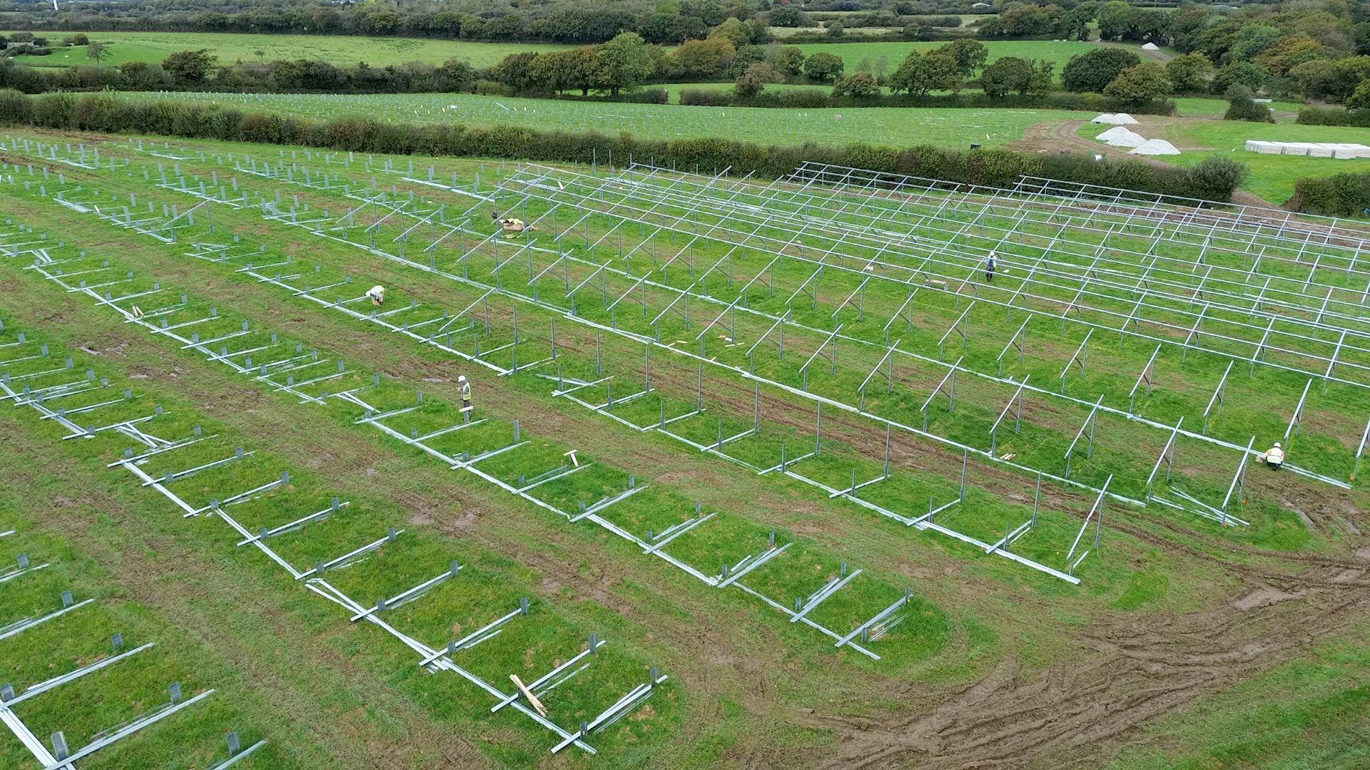 The view of an agricultural field from above, with workers laying out and erecting metal frames to hold solar panels