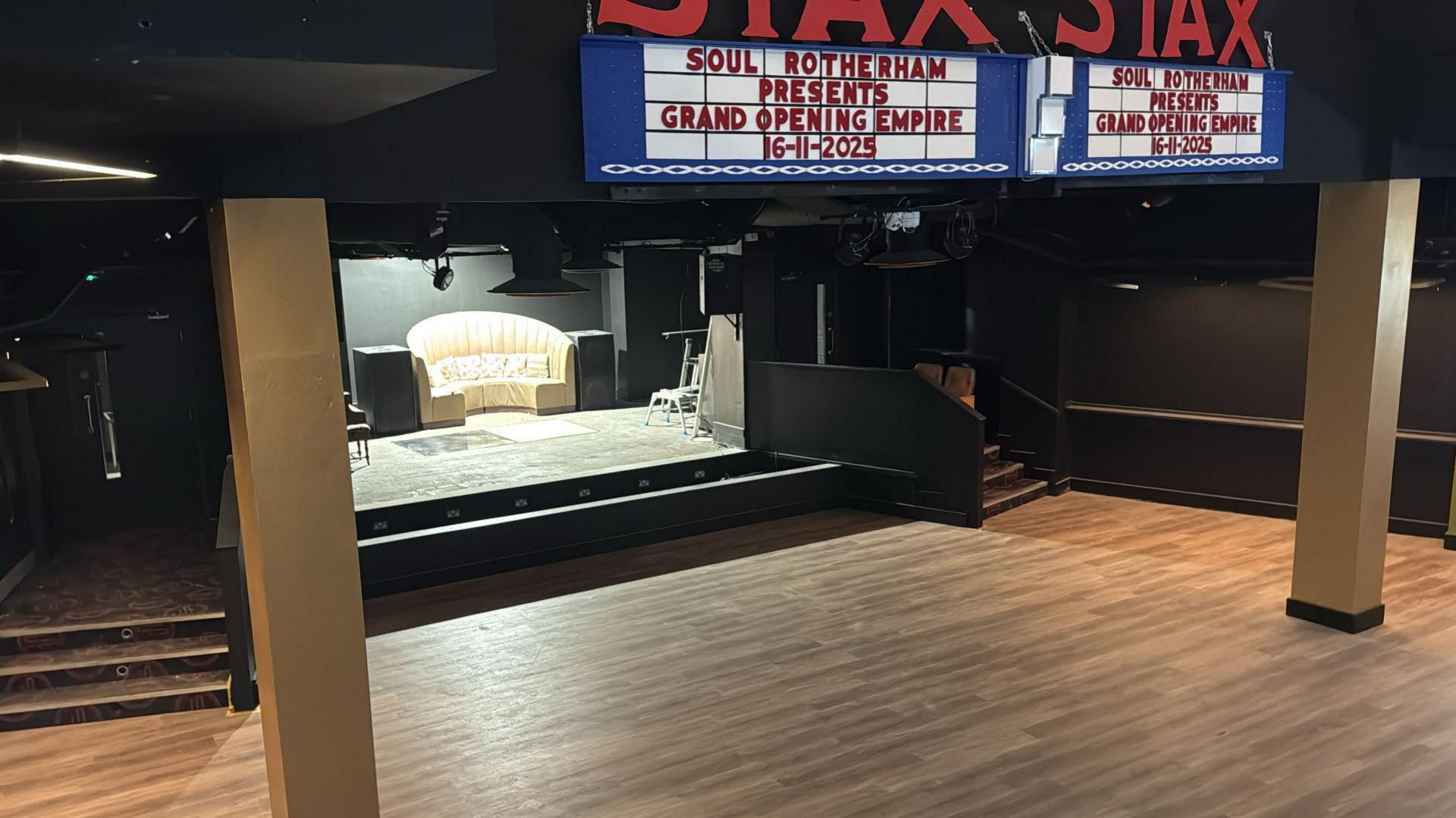 The inside of a music venue with a large wooden panelled dance floor and beams
