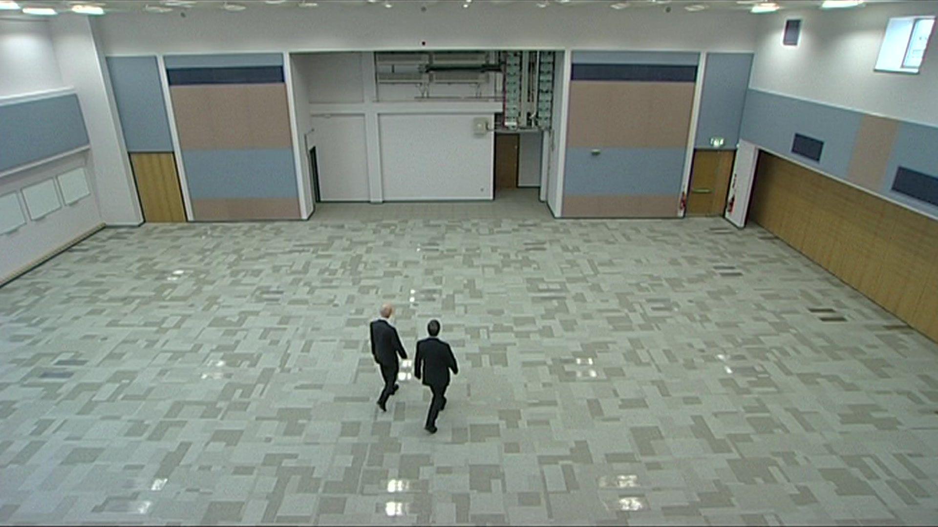 Two men walking through a vast empty space that had been planned as a control room