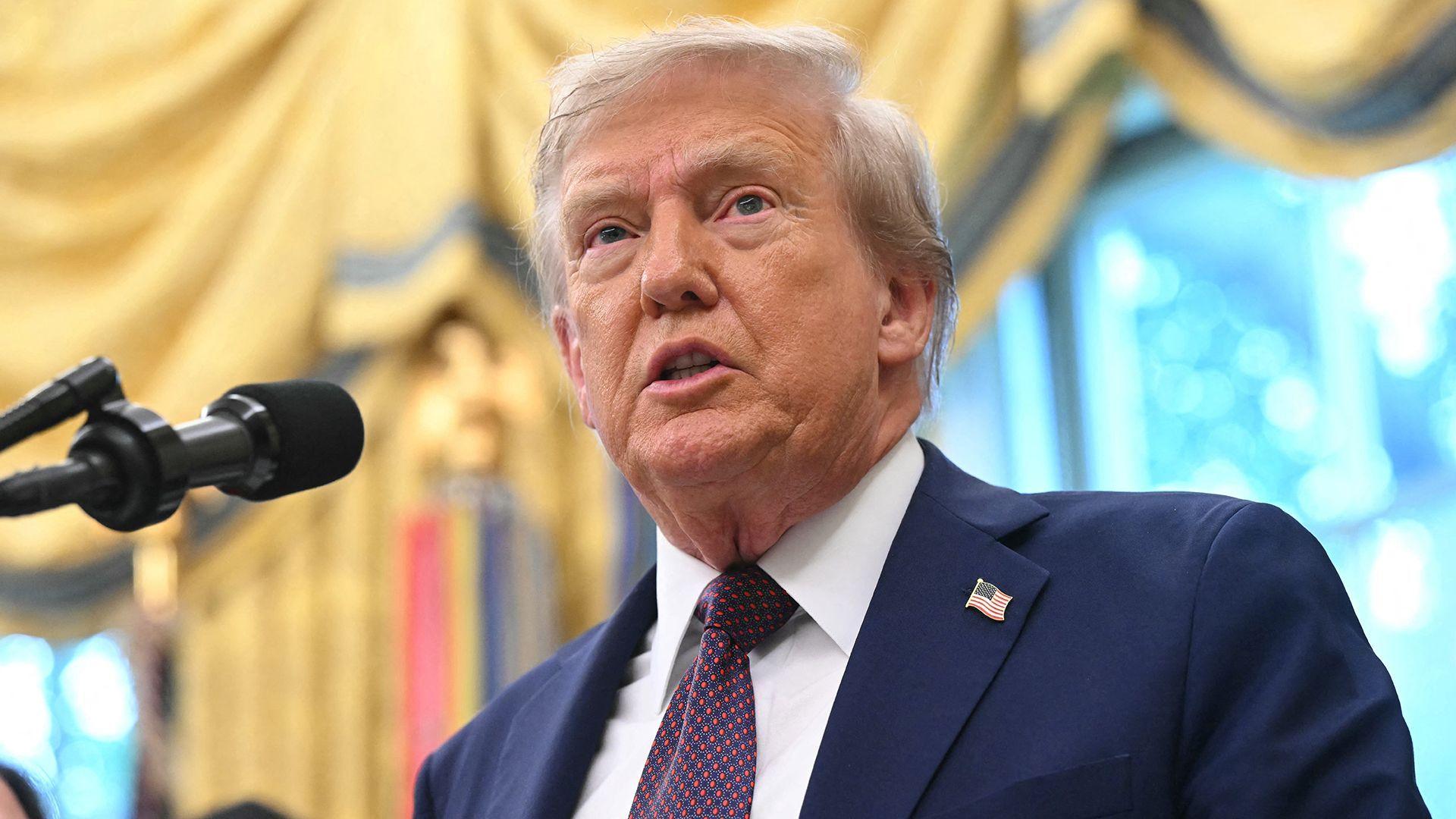 Donald Trump looks up while speaking into a microphone during a press briefing in the White House on 2 September, he's wearing a suit and tie with an American flag badge on his lapel.