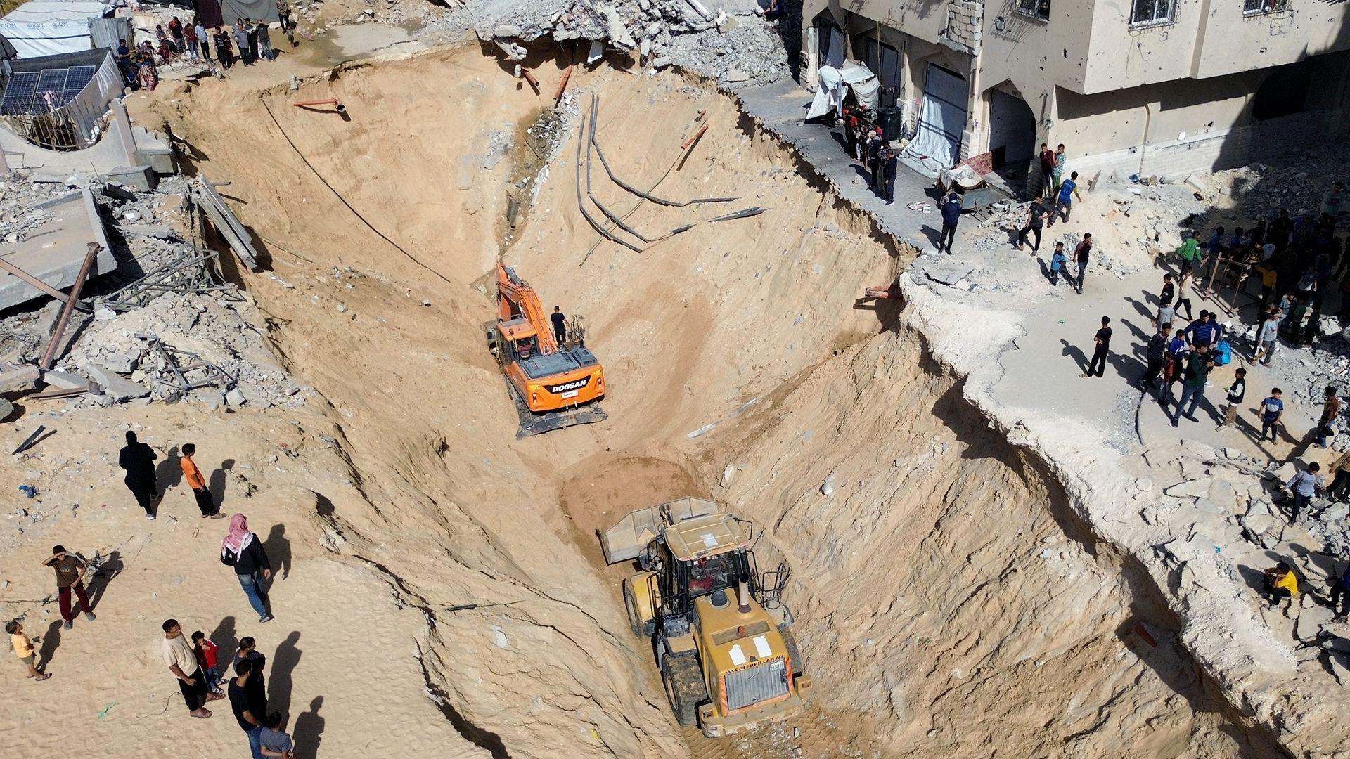 An aerial photo shows heavy excavating machinery is seen digging into a trench next to building rubble with people around it looking onduring an operation to look for bodies of Palestinians and Israeli hostages in Khan Younis on Tuesday.