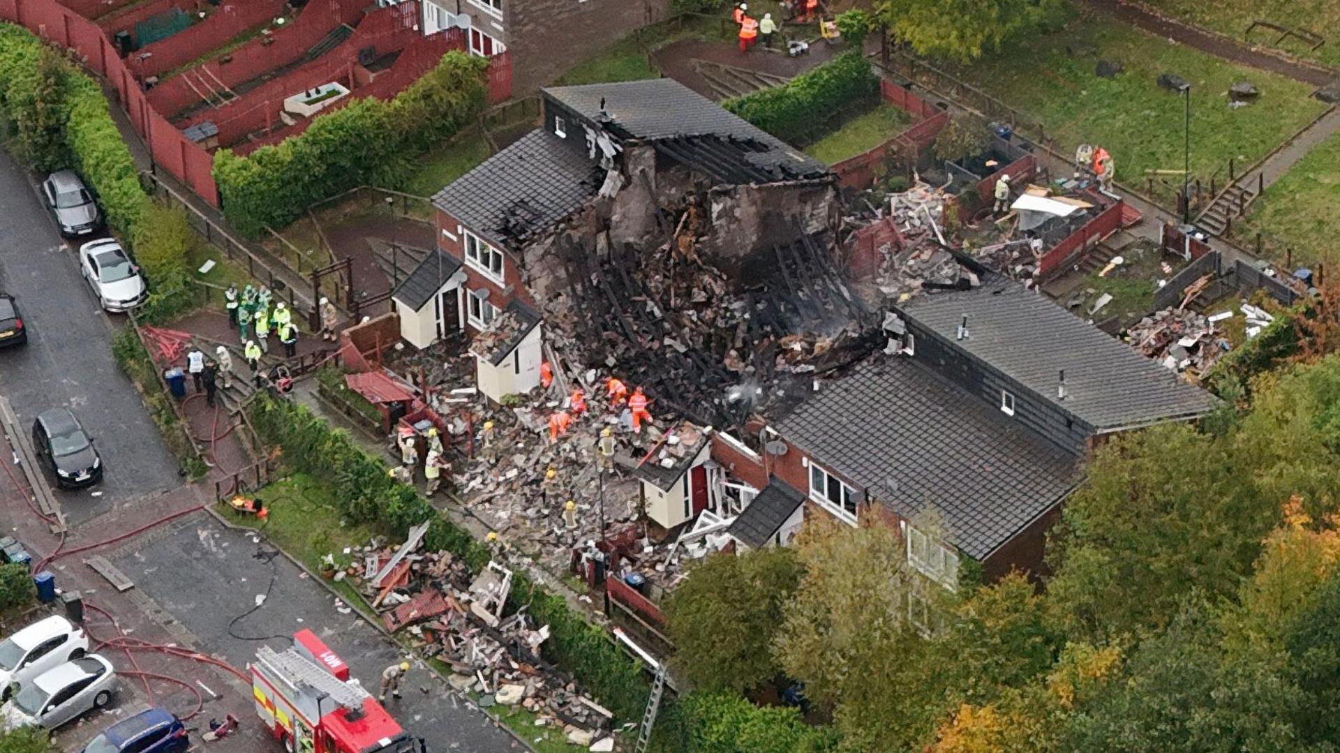 Firefighters on site at the explosion. The houses in the centre have been ripped apart and there is debris on the ground. 