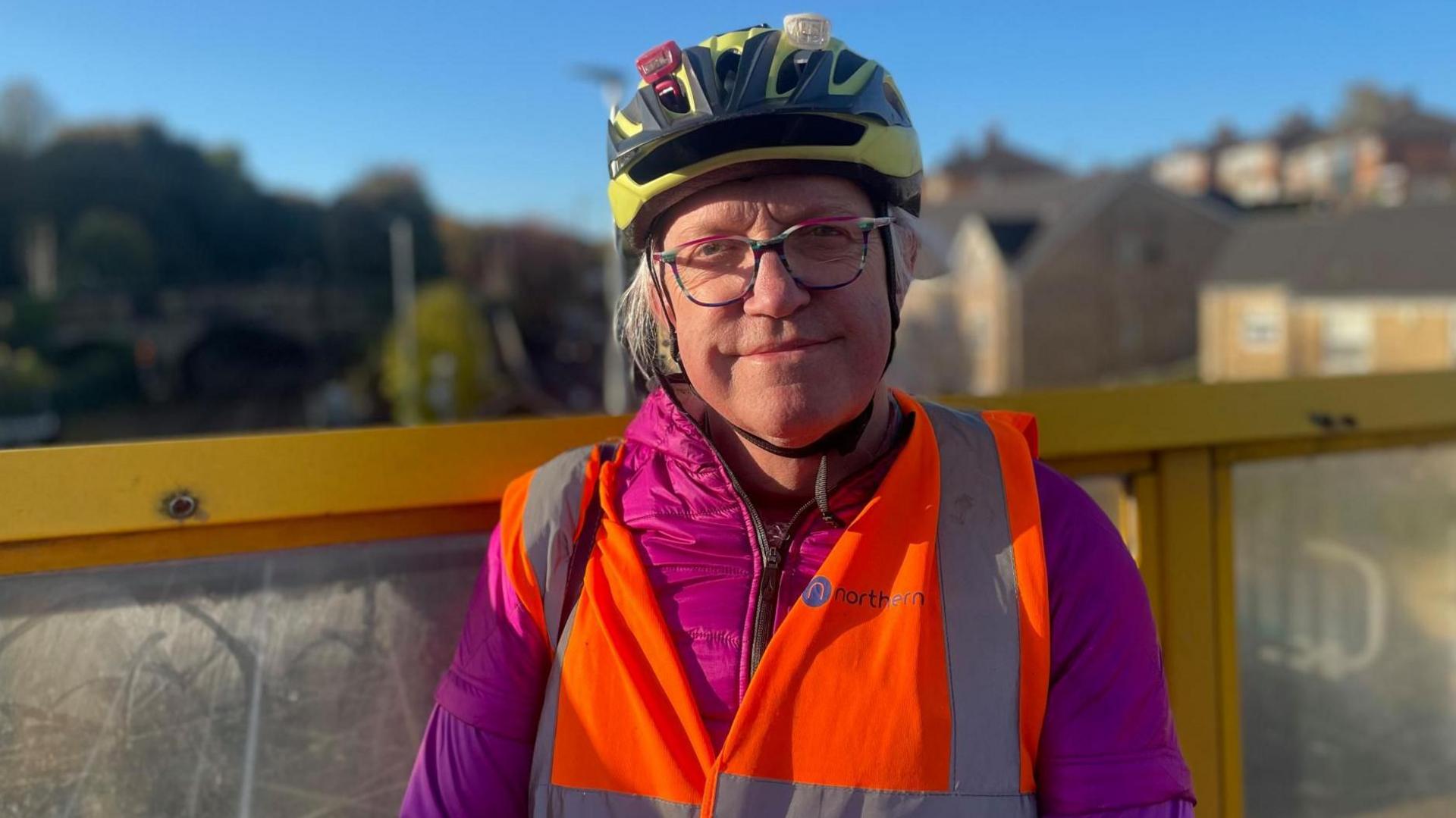 A man in a hugh vis jacket and cycling helmet stands on a railway bridge