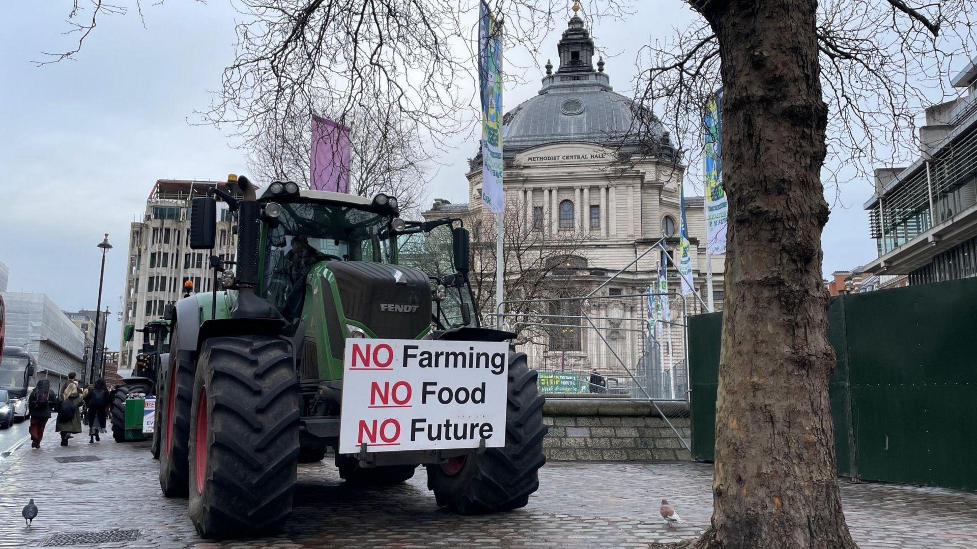 Tractors parked outside conference centre in a wet London street. The lead tractor has a placard which says "No Farming, No Food, No Future"