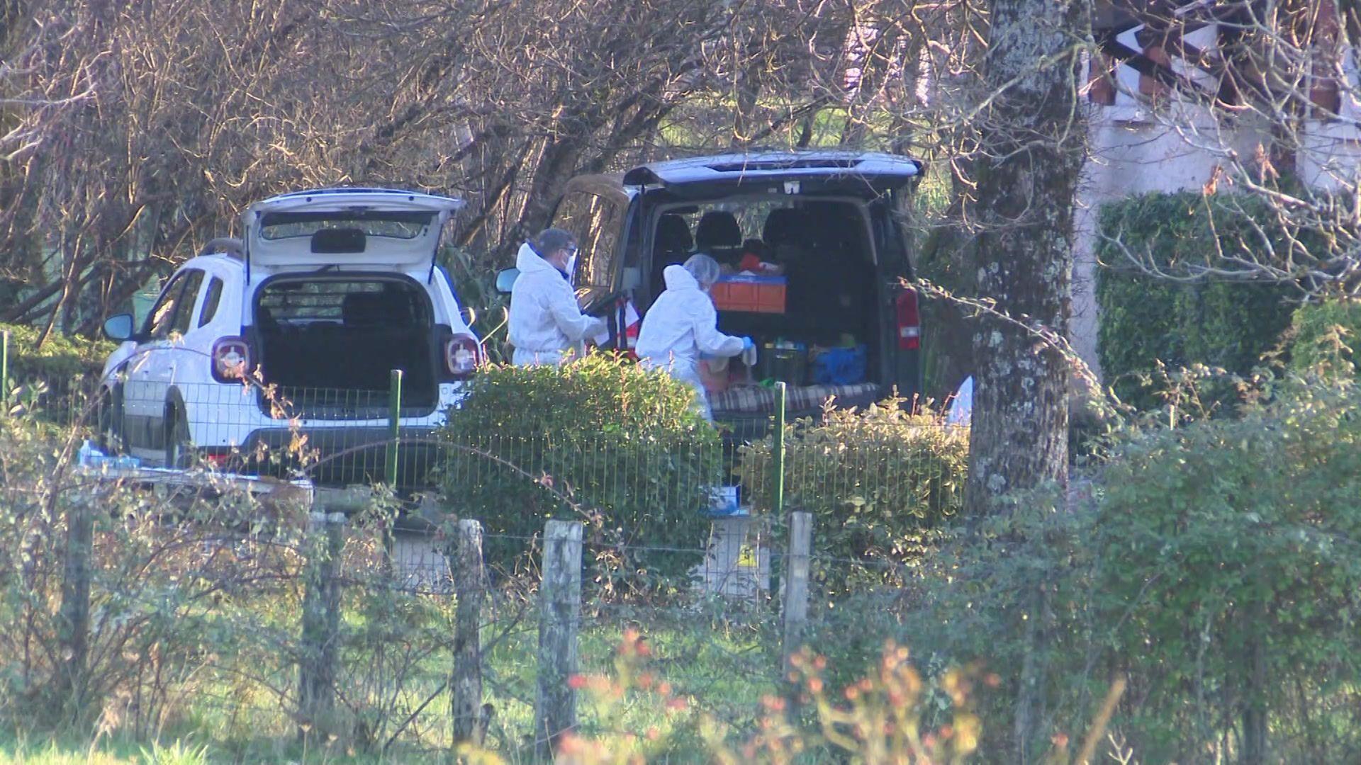 Forensics officers taking boxes either to or from the boots of a car, with another car with its boot open next to them. Trees and bushes are all around them.