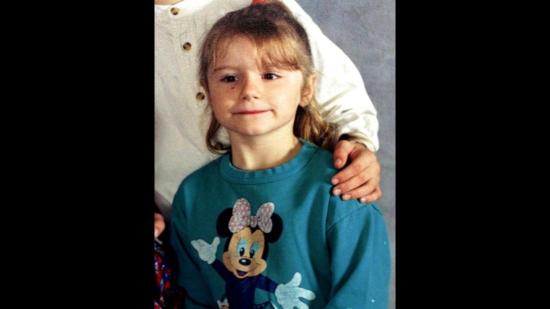 A blonde girl in a teal-coloured jumper and with a picture of Minnie Mouse. 
