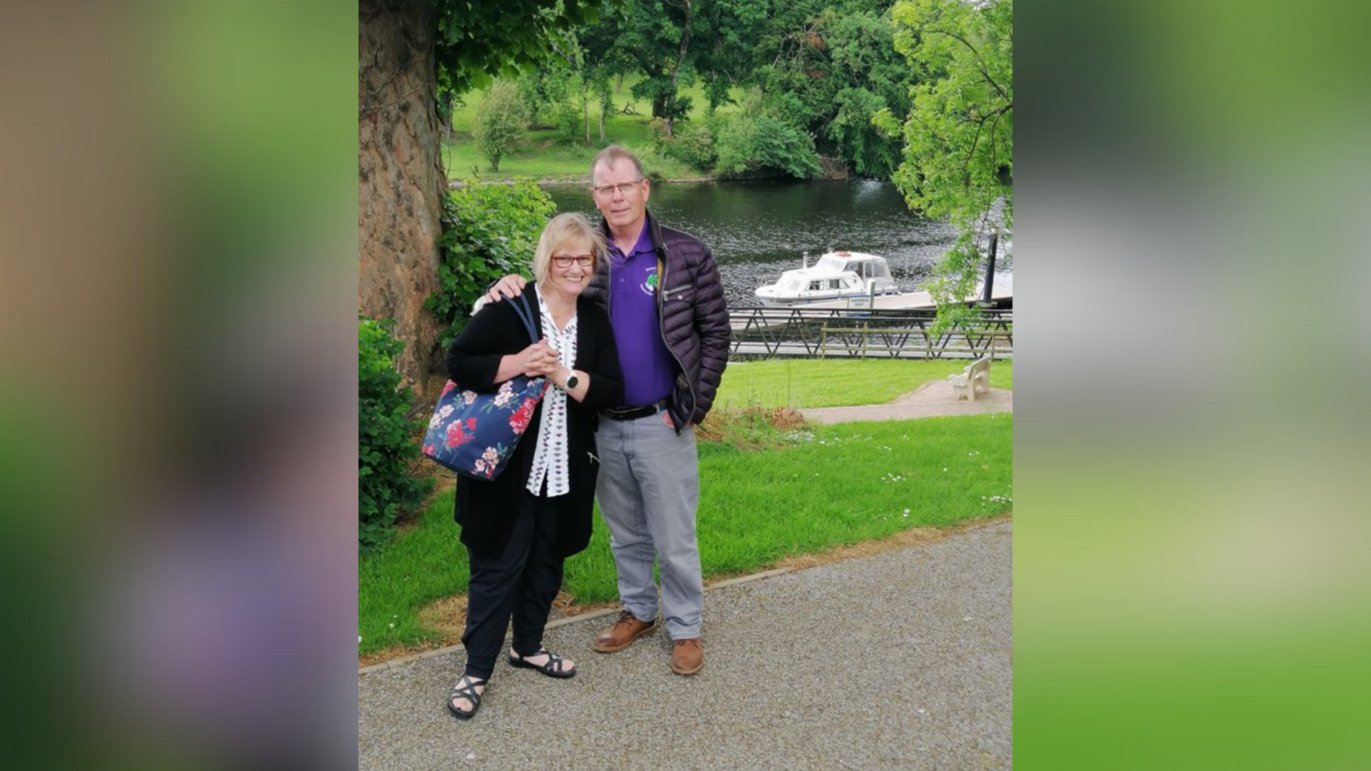 The McMillans standing by a river. There are trees and a boat behind them.
