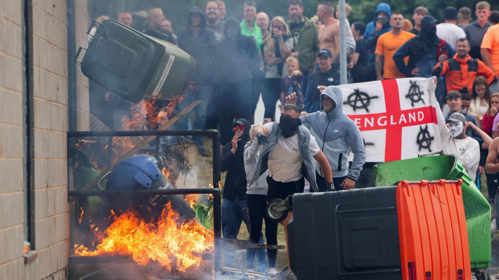 More than 30 rioters can be seen wearing masks or face coverings as a bin is thrown at a fire outside the hotel. 