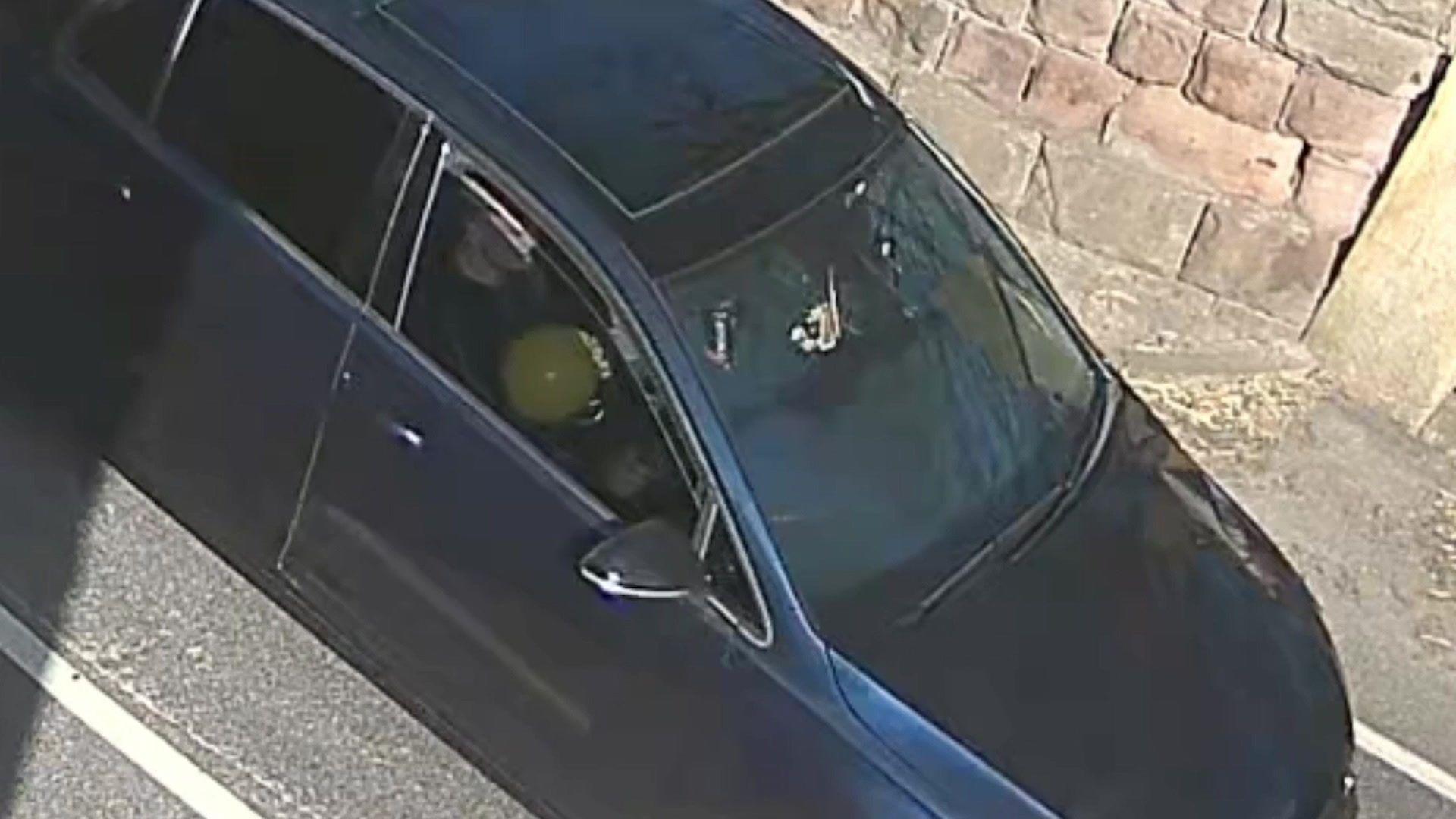 A CCTV image shows the side of a black VW car as it passes the camera. Through the front driver's side window a man can be seen holding an inflated yellow balloon.