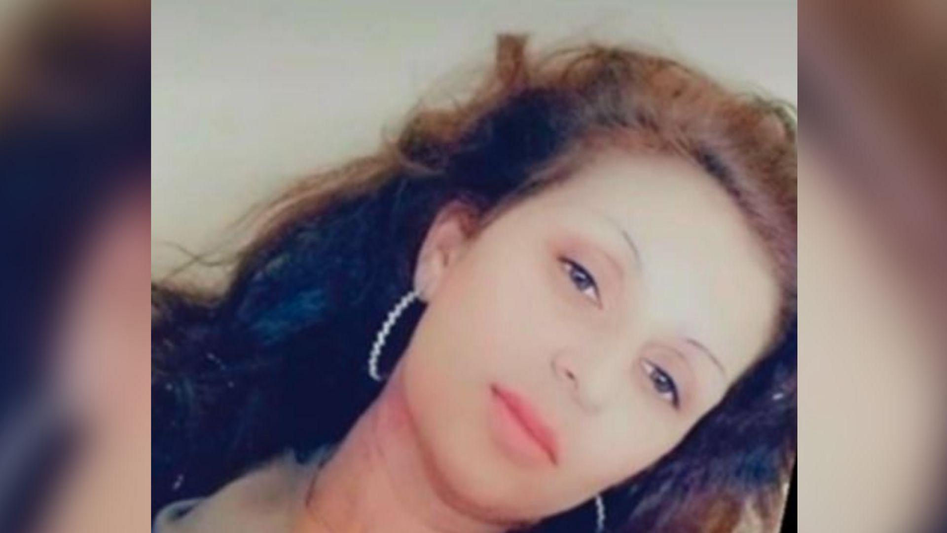 A woman in her 30s with long brown hair. She is wearing large hooped white earrings.