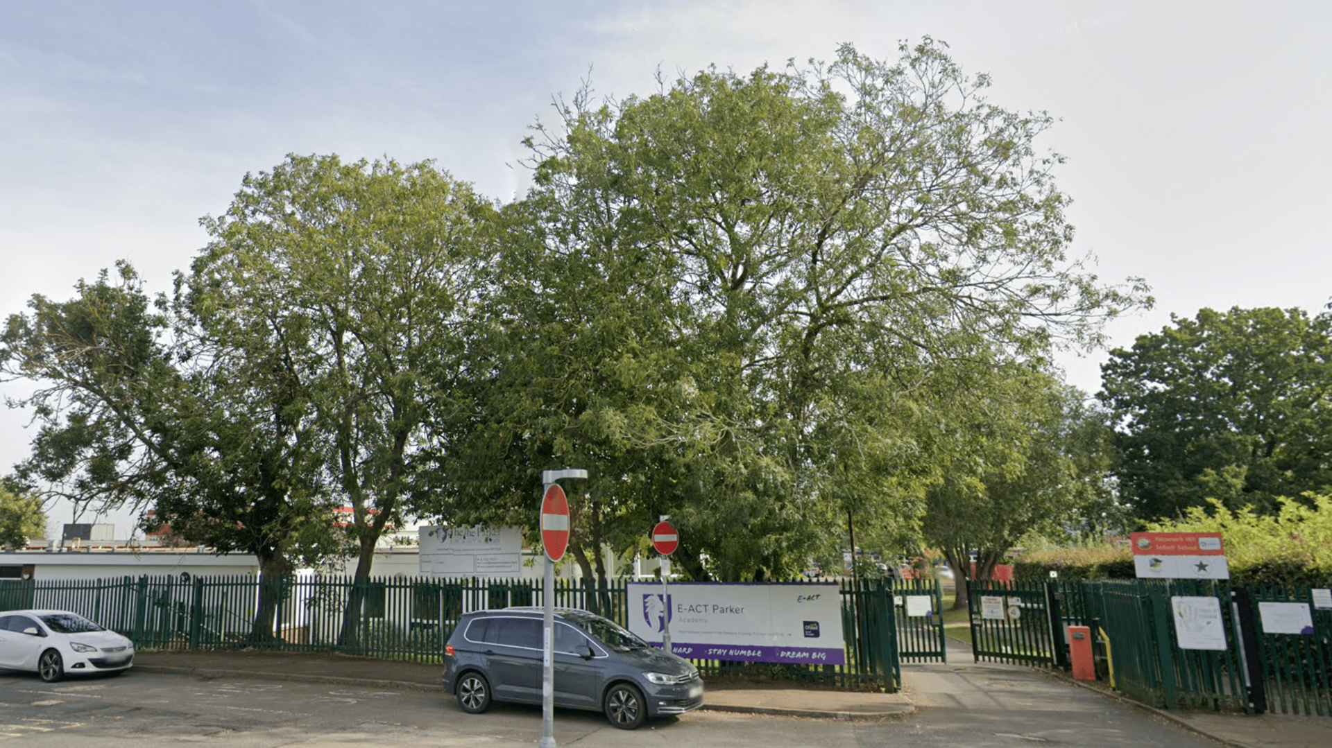 A photo of the front of the E-ACT Parker Academy school building surrounded by trees, cars and street signs. 