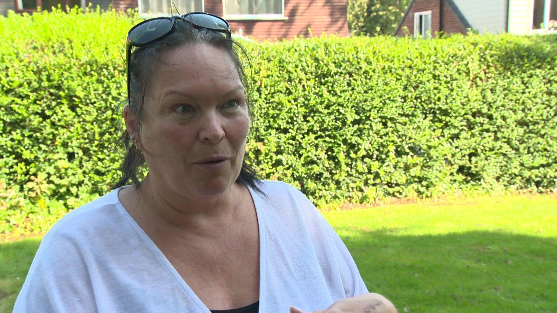 Gillian looks just to the left of the camera as she talks to a BBC reporter close to a mass grave, wearing a white blouse and black top, with sunglasses on her head. 