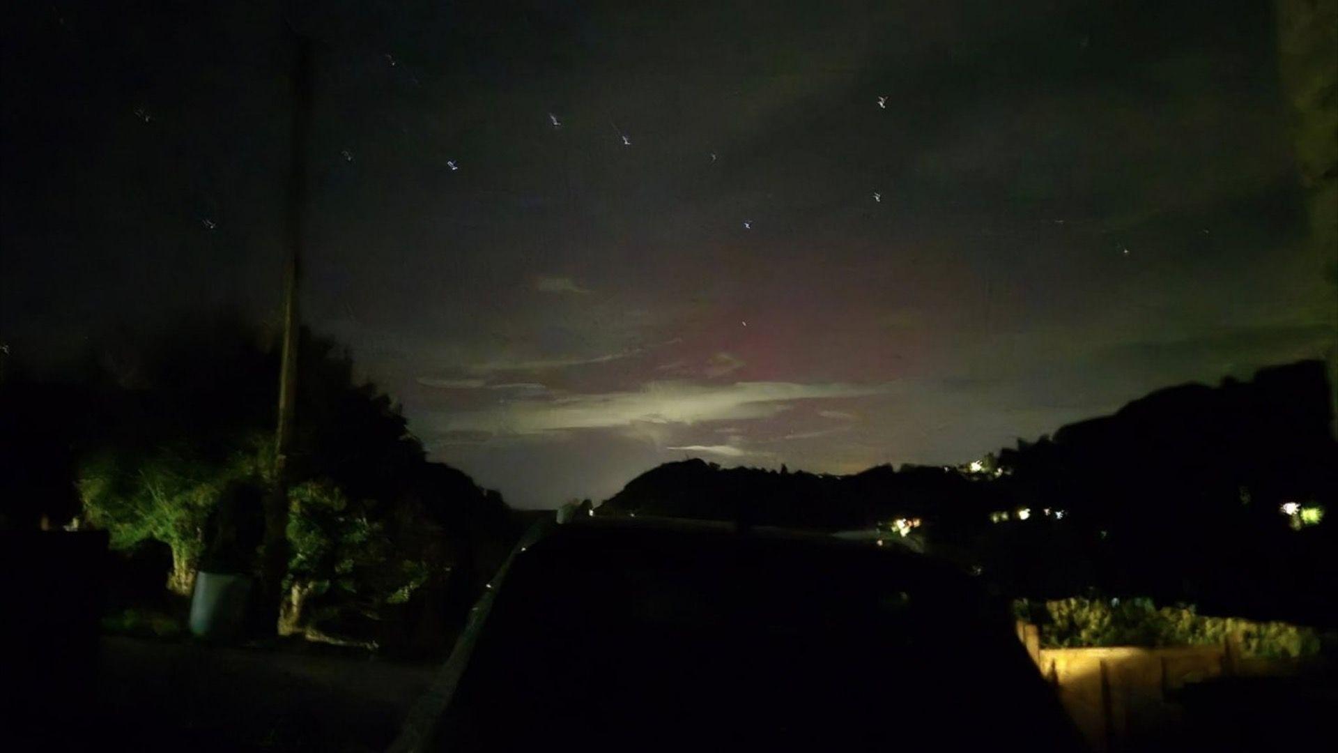 A night sky with the northern lights around it and a dark shadow of trees amongst it.