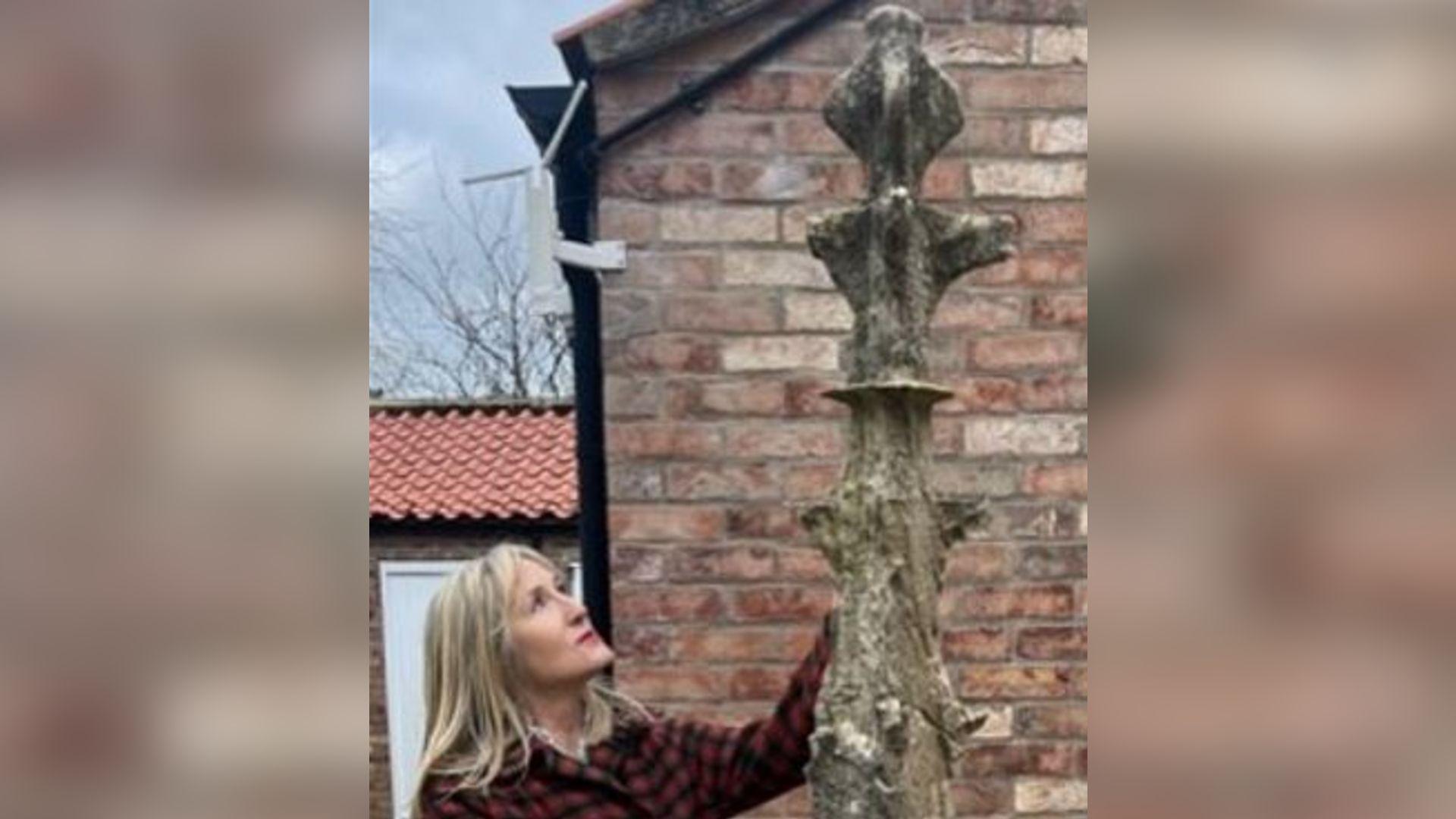 A woman stands next to a stone pinnacle, which is towering above her.