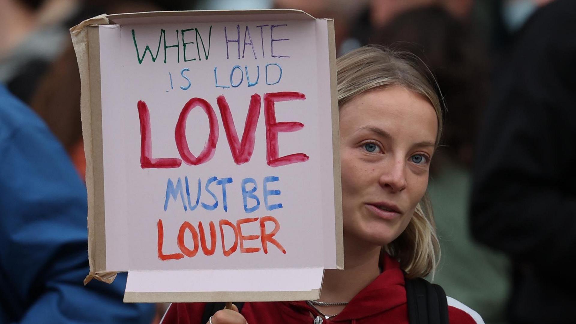 woman holds placard saying "when hate is loud, love must be louder"