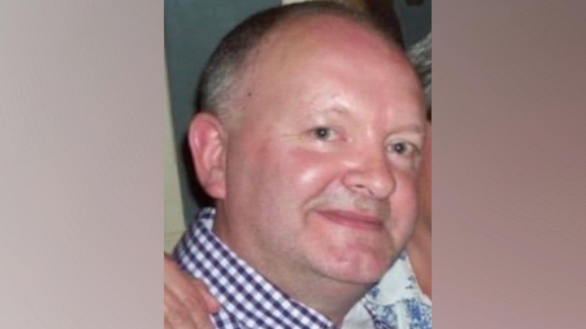 A picture of Michael Nolan who died aged 63 in a mental health unit in Essex. He is wearing a navy and white checked shirt and has blue eyes. The picture shows his head and shoulders and he is looking at the camera smiling.