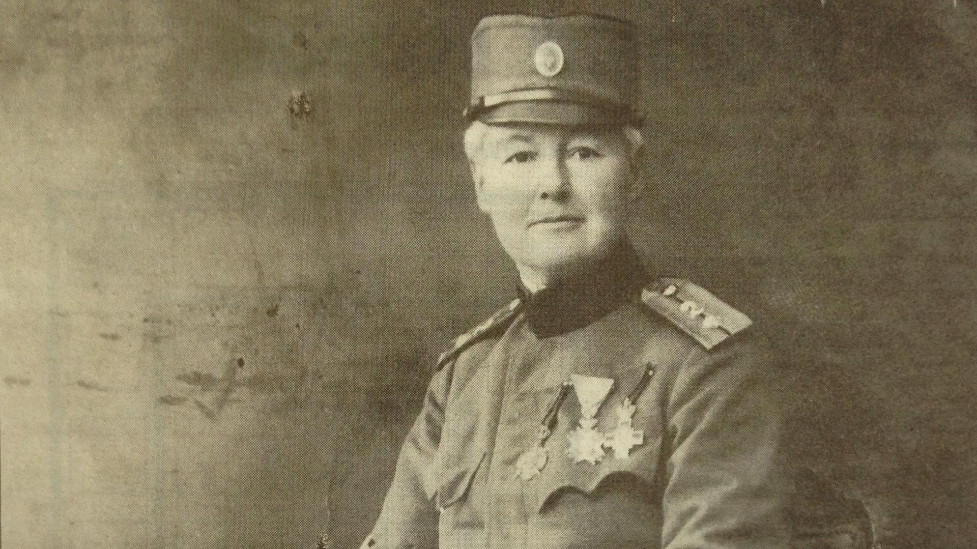 A portrait style image of Flora Sandes. She is facing the camera with a slight smile on her face. She is in her army uniform with several army badges of honour on the left hand side of her chest.