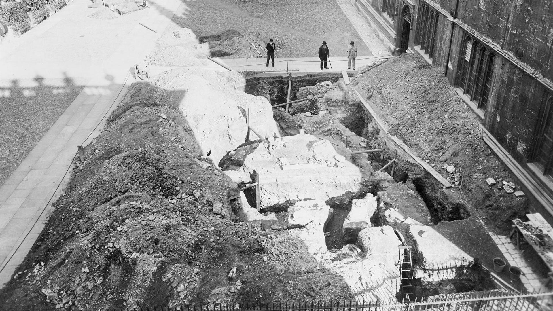 The remains of Oxford's boundary among rubble and building works in a black and white 19th Century photo. Men in Victorian clothes and hats are visible, one with a cane.