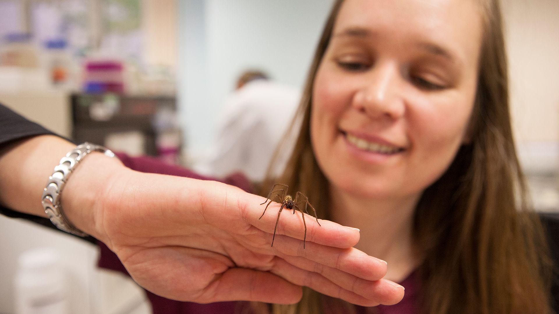 A woman holds a spider in her hand and smiles in a lab