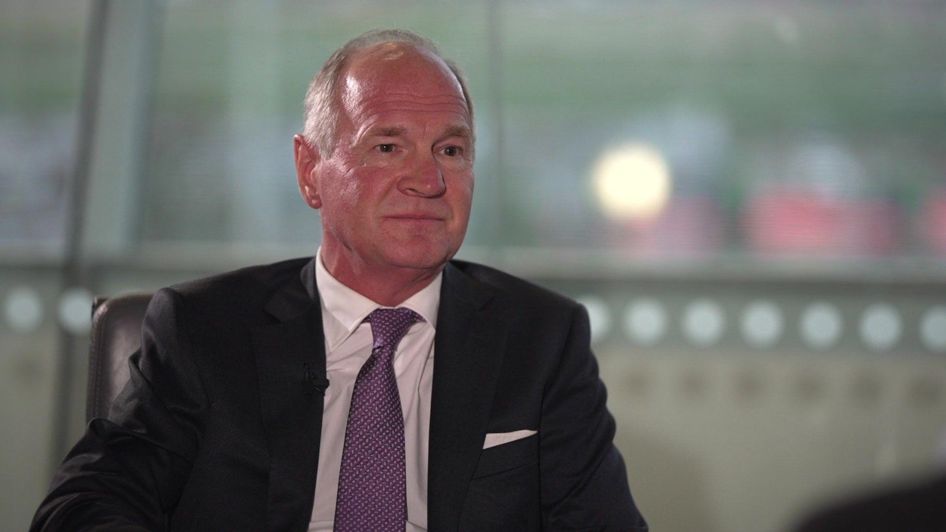 Thomas Woldbye, the boss of Heathrow Airport, sitting and talking, wearing a light coloured shirt, a dark coloured jacket and a purple tie.