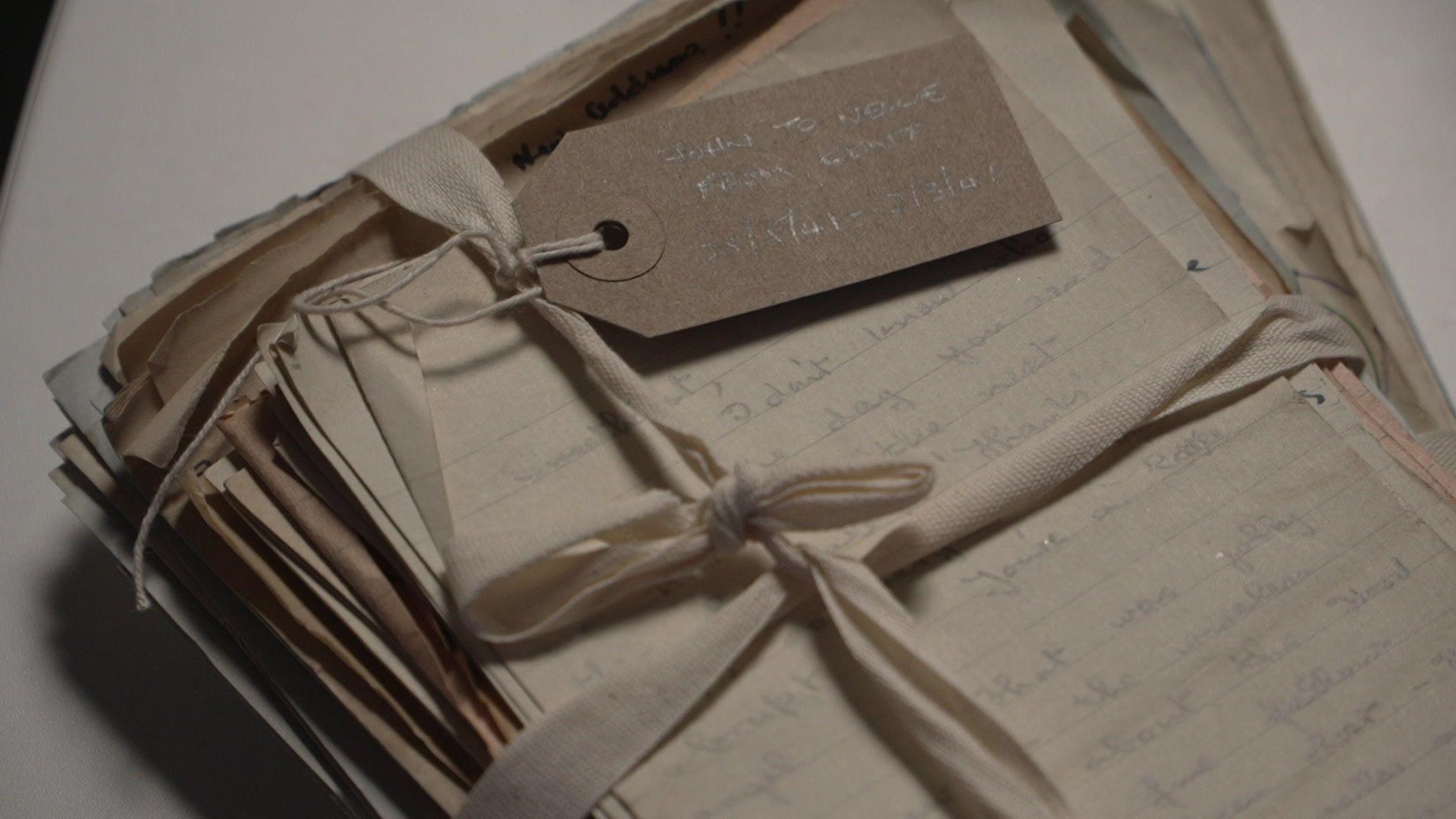 A stack of hand-written letters all kept together by a white bow tied around them.