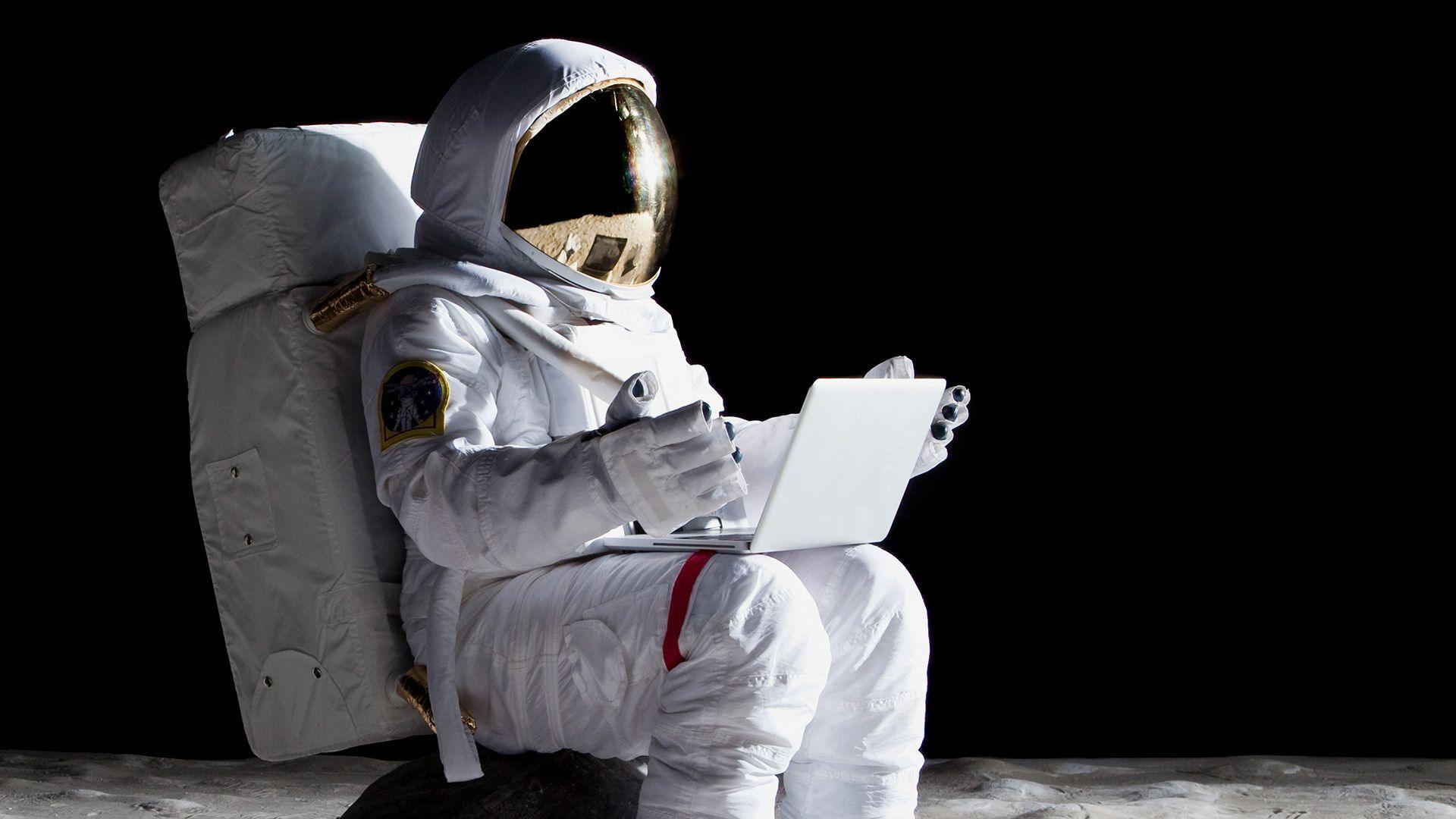 An astronaut sat on the moon, holding a laptop