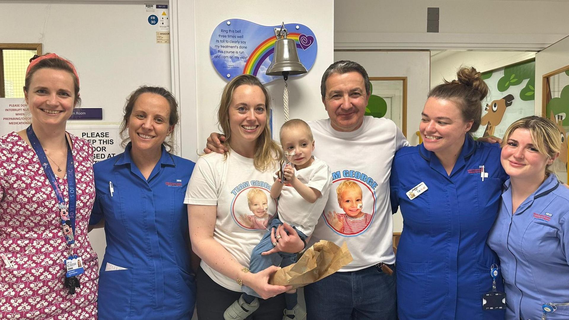 George is held by his mother, and is next to his father in a group photo with hospital staff.