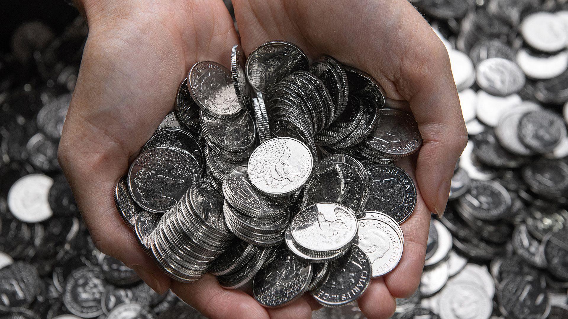 A hand with a pile of 10p coins on a background of the same coins