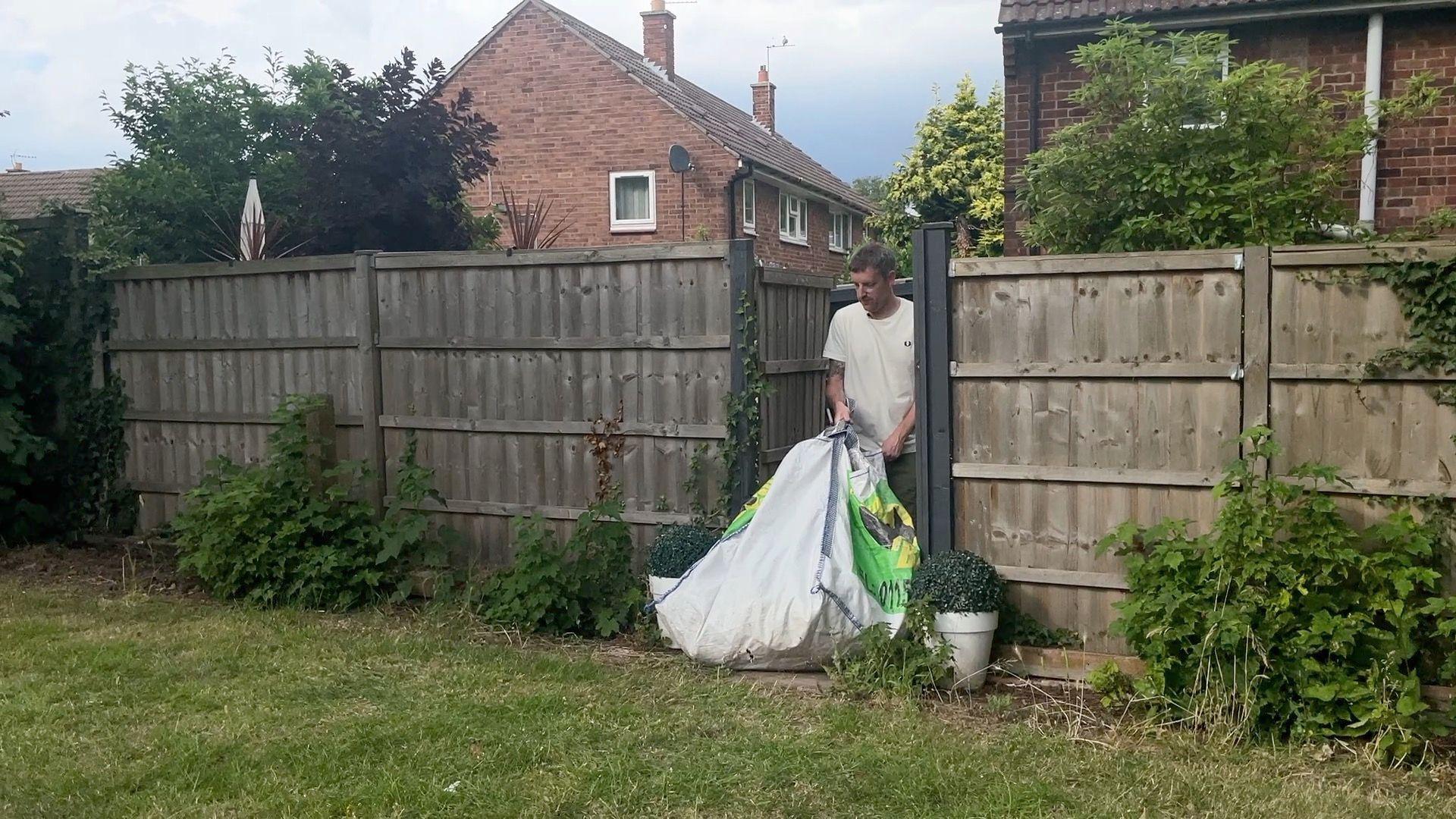 Adam Castledine taking a bag of garden waste out of his garden and on to a grass verge