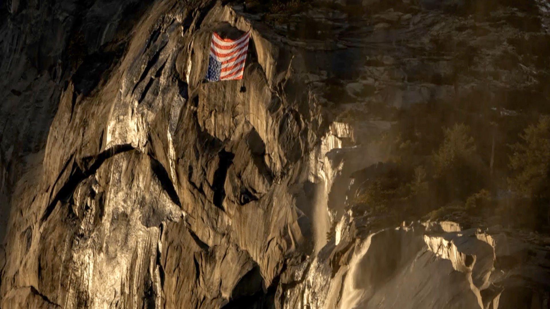 Un upside down American Flag hangs on the face of a rock formation at dusk