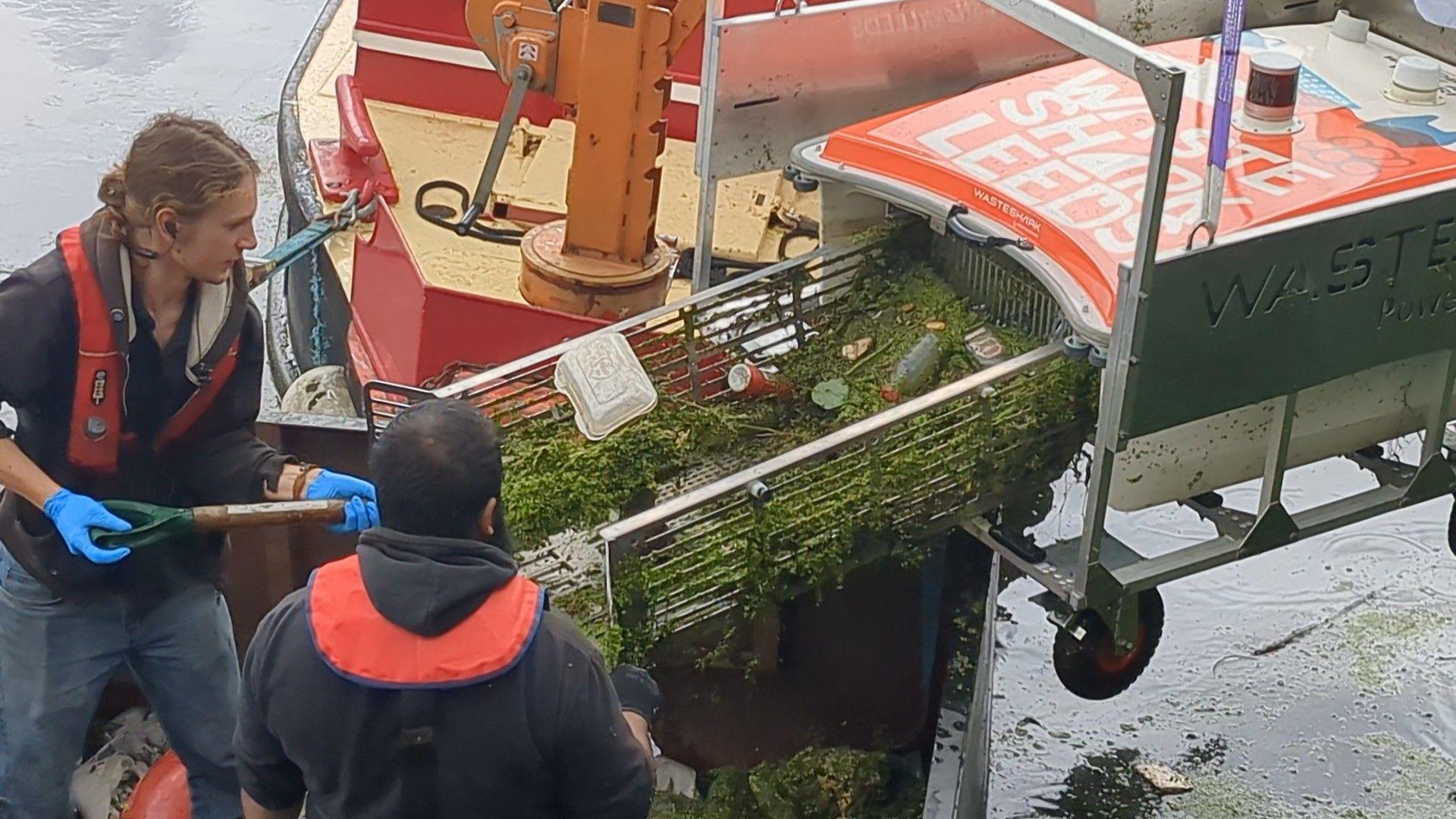Two people help remove debris and rubbish from a machine used to clear waste the waterways in Leeds.