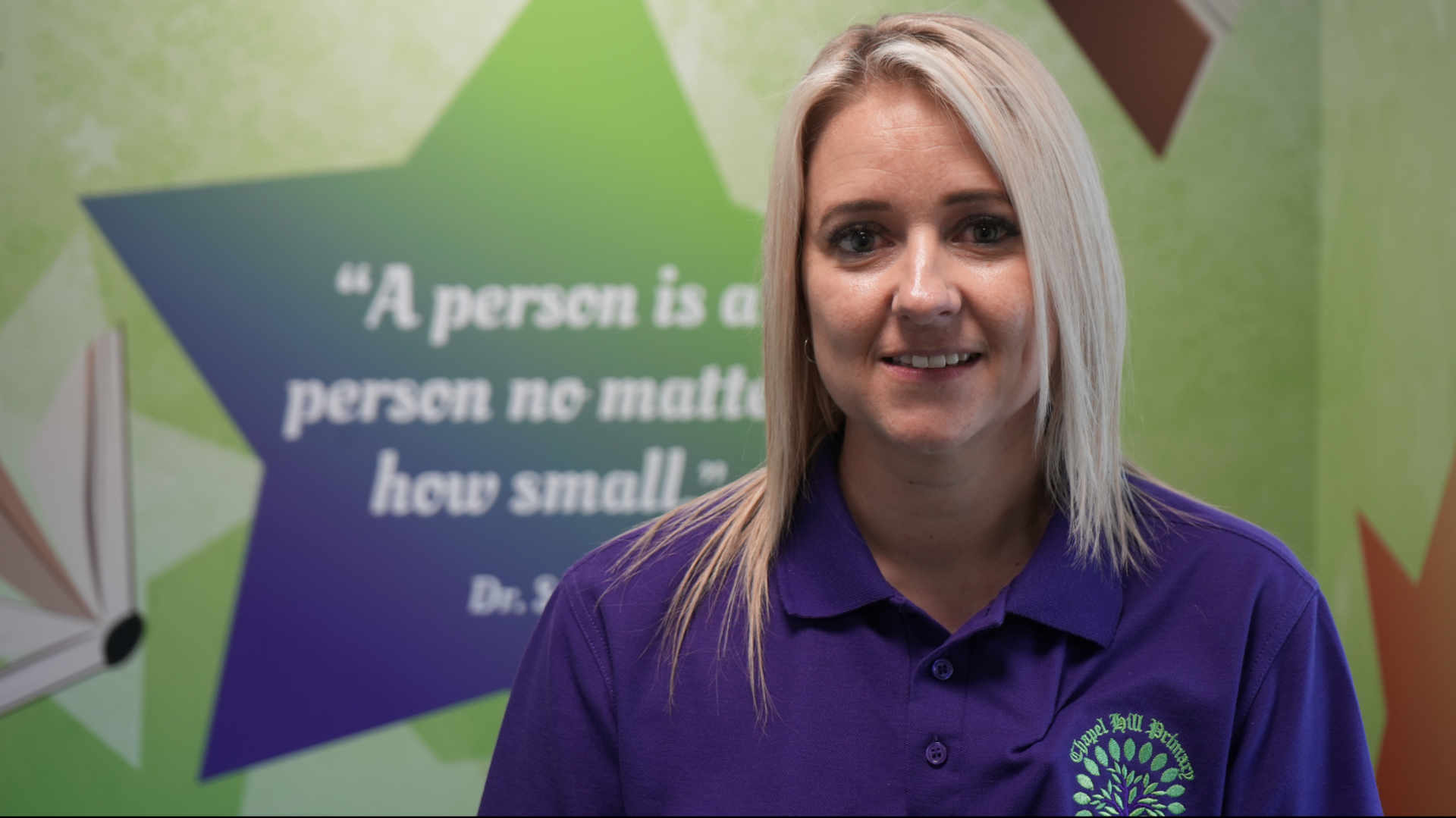 Claire Good is wearing a purple polo shirt with a green Chapel Hill Primary logo on it. She is smiling at the camera.