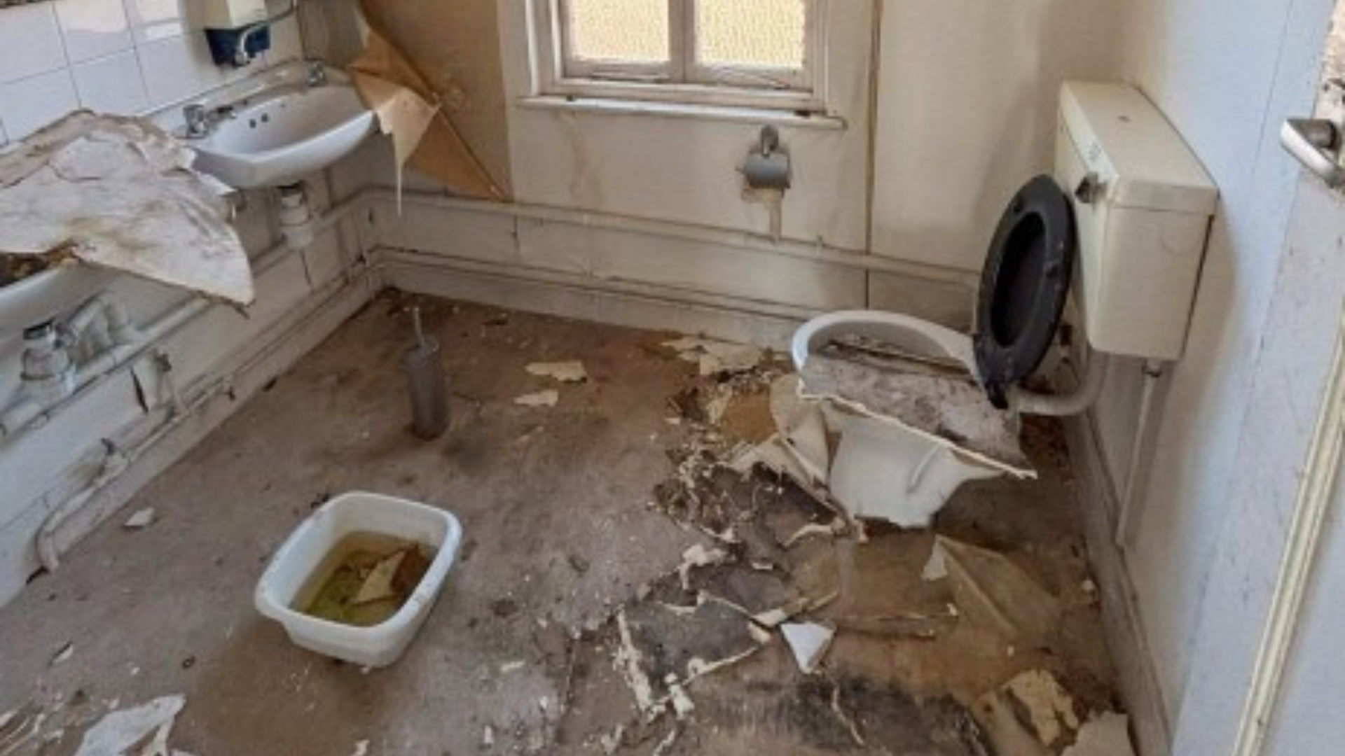 The bathroom of the former office in Cheriton Place in Folkestone. Wallpaper is ripped, with debris scattered across the floor.