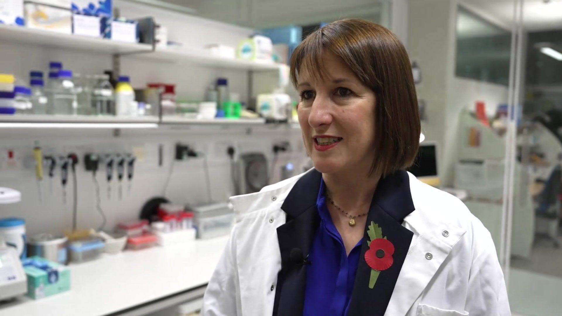 Rachel Reeves in a lab wearing a white lab coat. She is wearing a poppy on the lapel of a navy blazer she is wearing beneath the coat