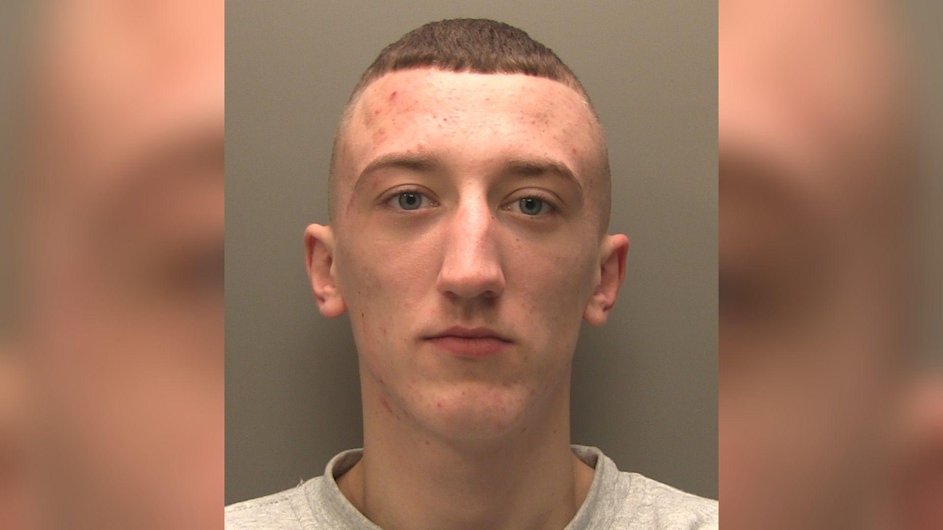 A police-issued custody image of a man with cropped brown hair wearing a grey sweatshirt