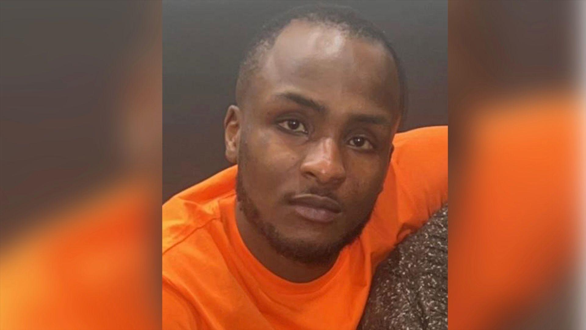 Sanchini Thompson looks at camera. He is wearing an orange T-shirt and has a short beard around his chin